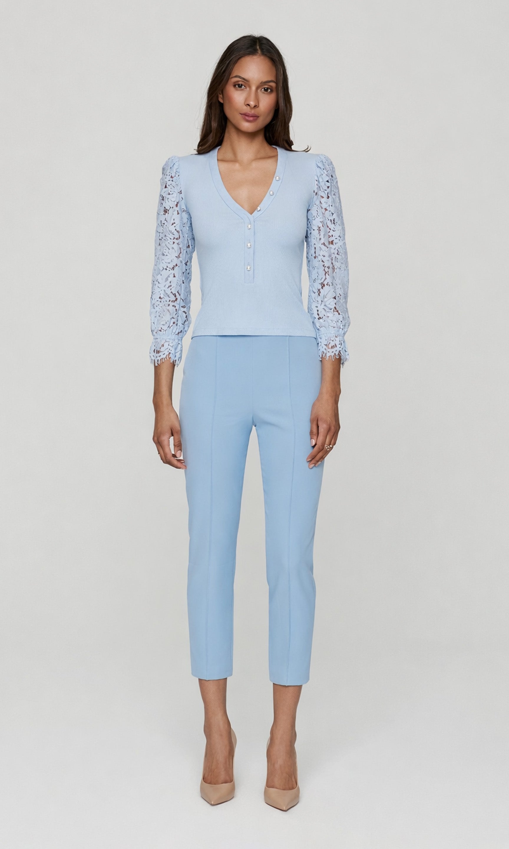 Full body image of woman wearing a light blue top with lace sleeves and matching blue pants on a plain background