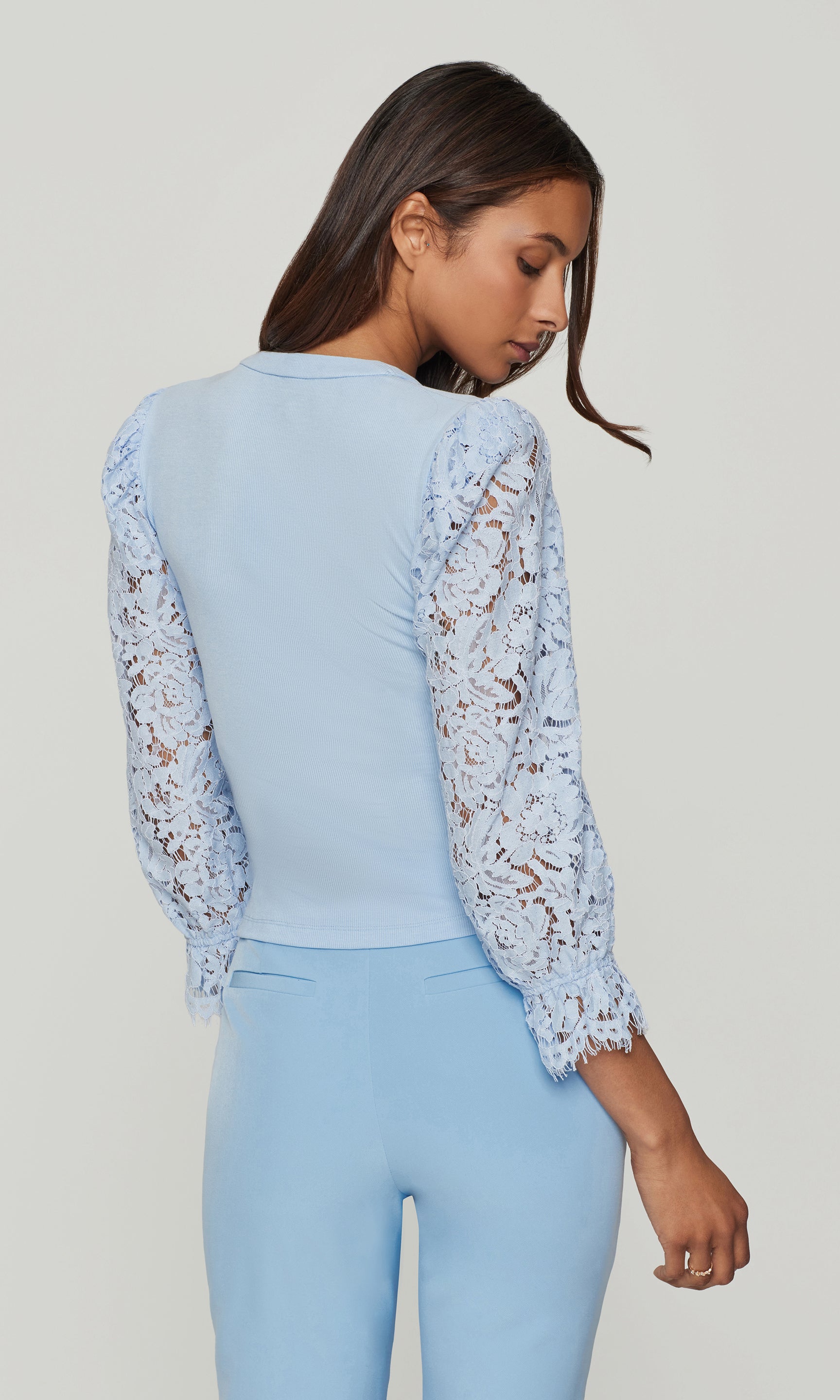 Back view of woman wearing a light blue top with lace sleeves and matching blue pants on a plain background