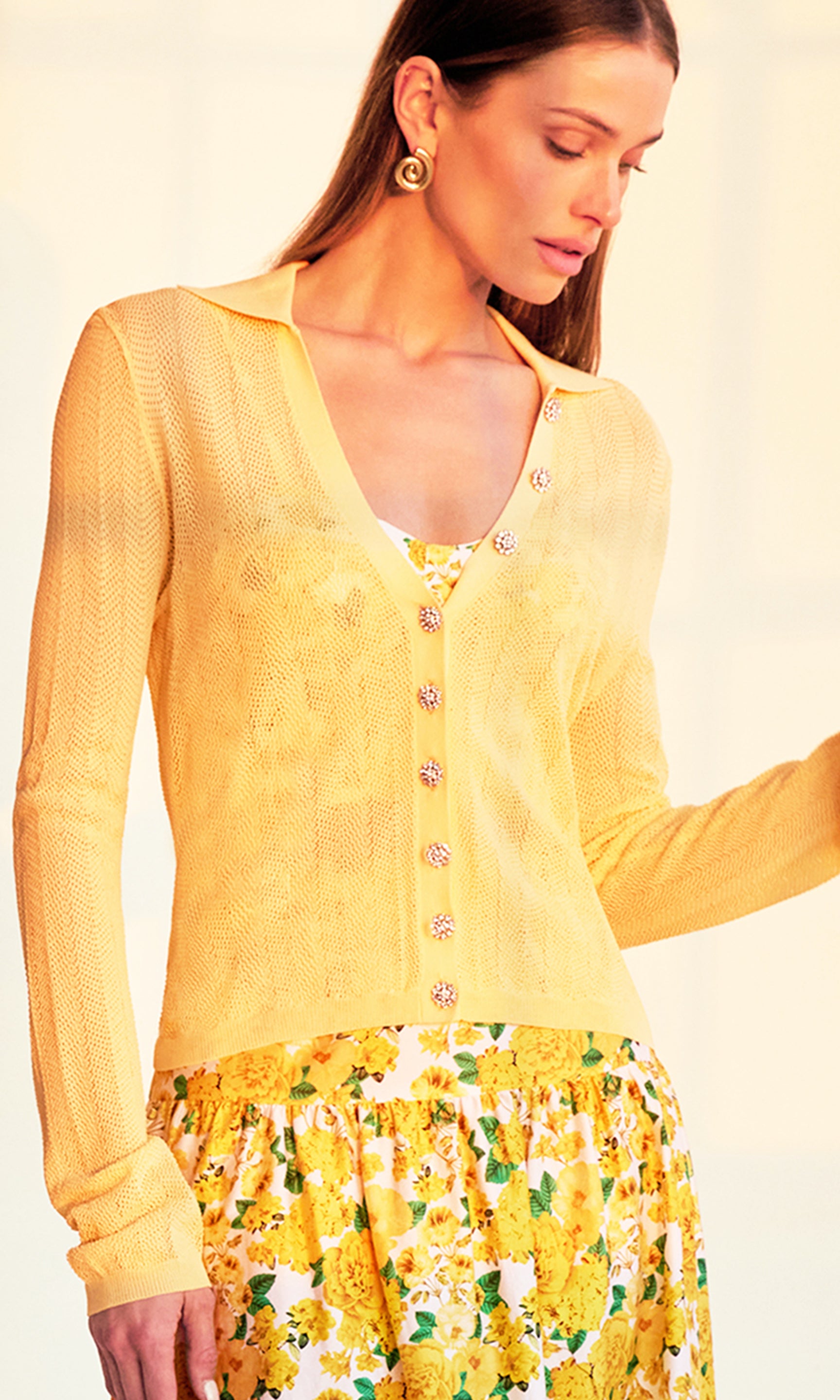 zoomed in image of model in a sunset-lit room wearing the Megan Pointelle Cardigan in pale yellow showing the crystal buttons over a yellow floral top and skirt.