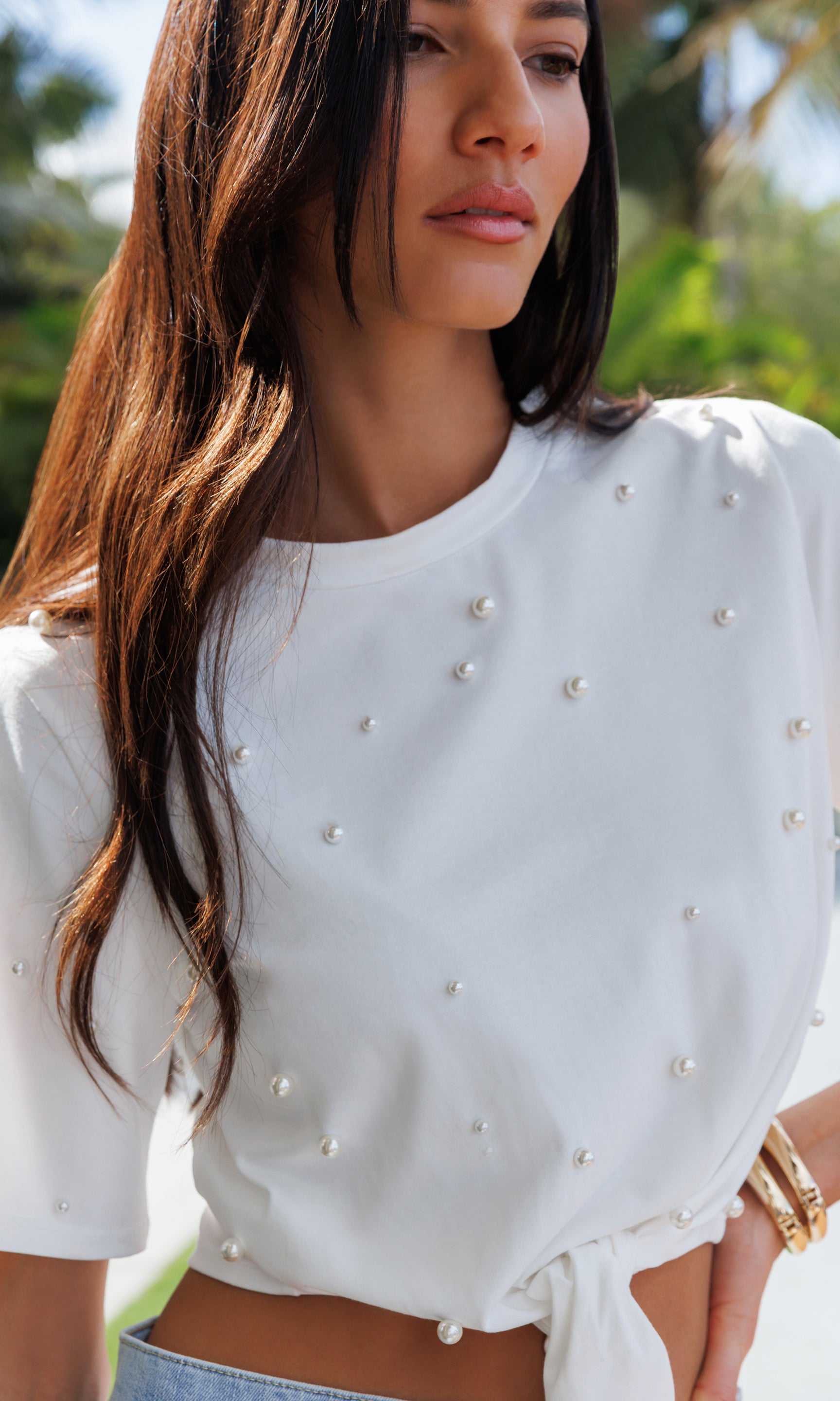 Woman wearing a white top with pearl embellishments outdoors