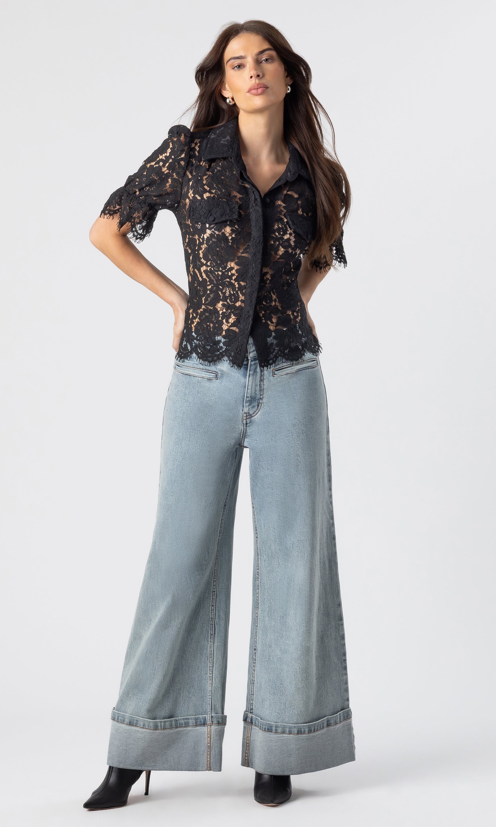 Model stands wearing a black lace short sleeve top with cuffed flare jeans and black booties