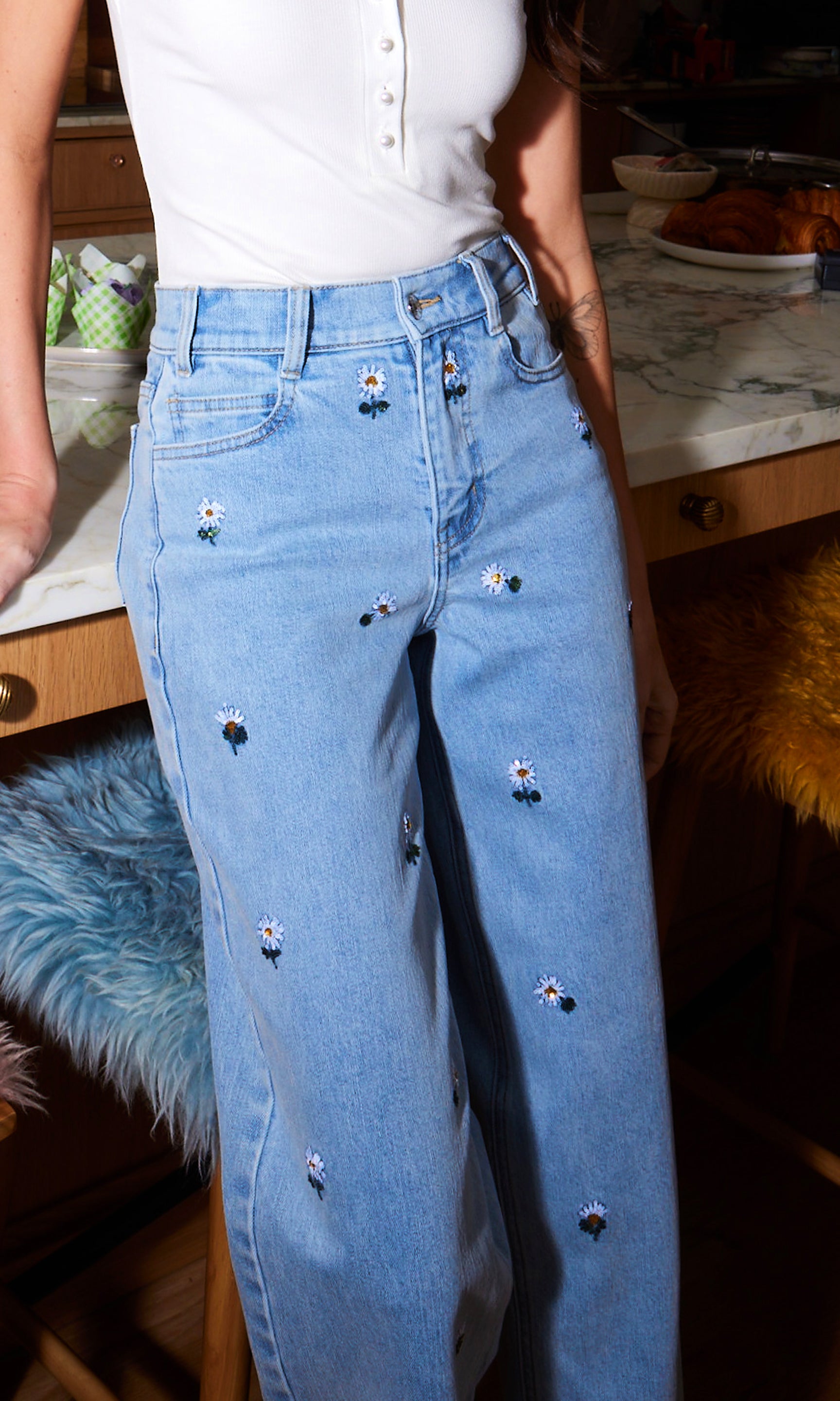 Light blue jeans with decorative daisy embroidery worn by a person in an indoor setting.