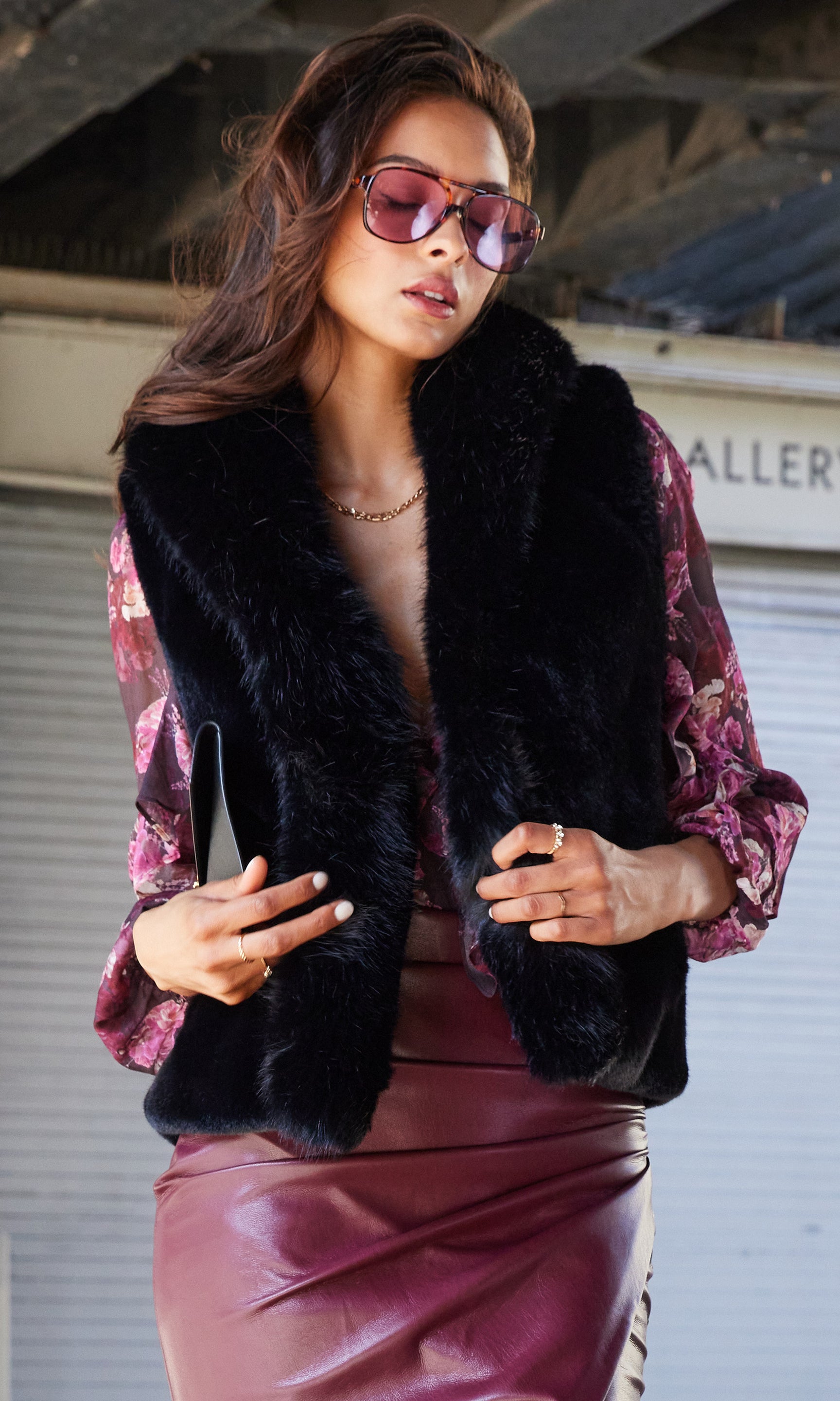 Woman wearing a black fur vest over a pink floral blouse with a pink skirt.