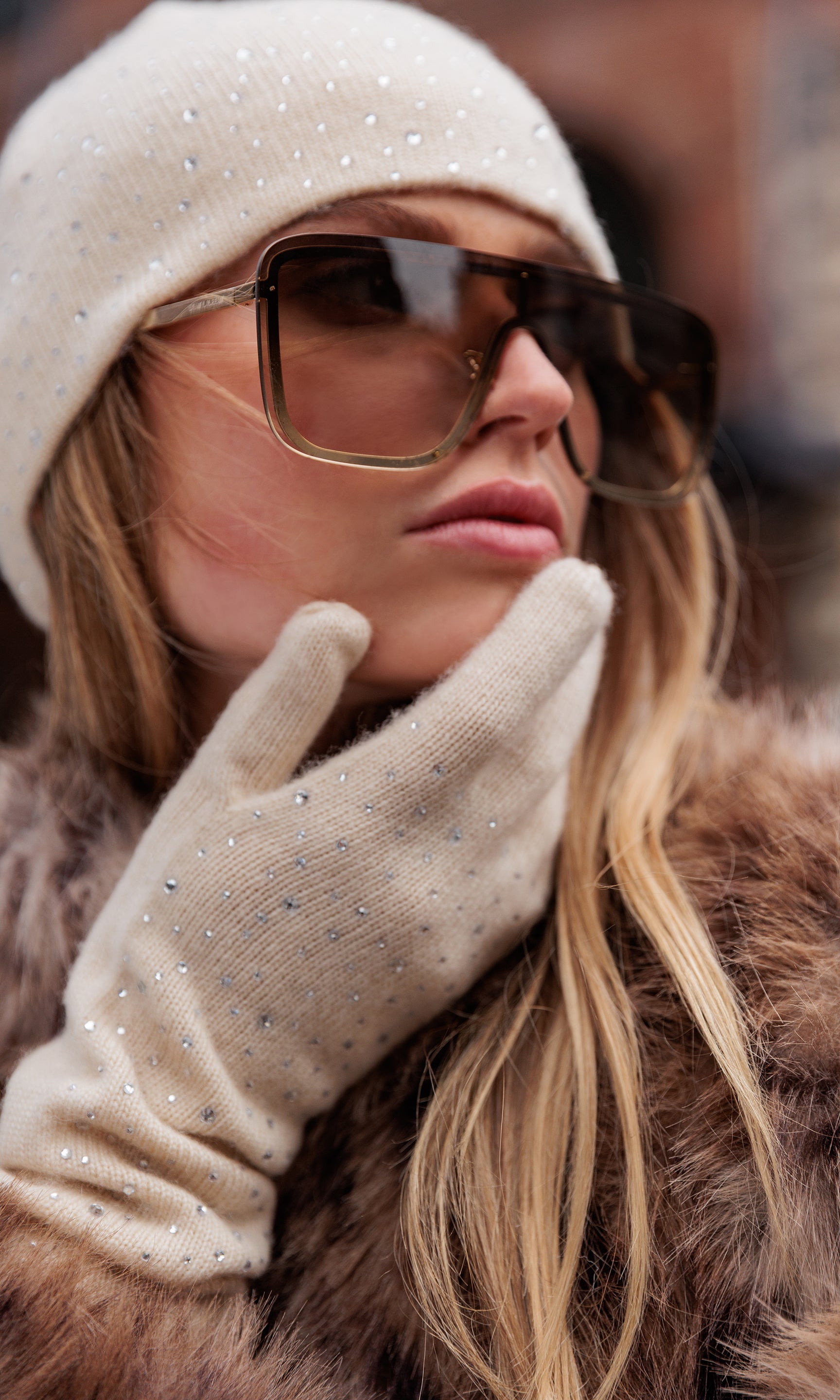 Woman wearing sunglasses, a beanie, and gloves in a winter setting