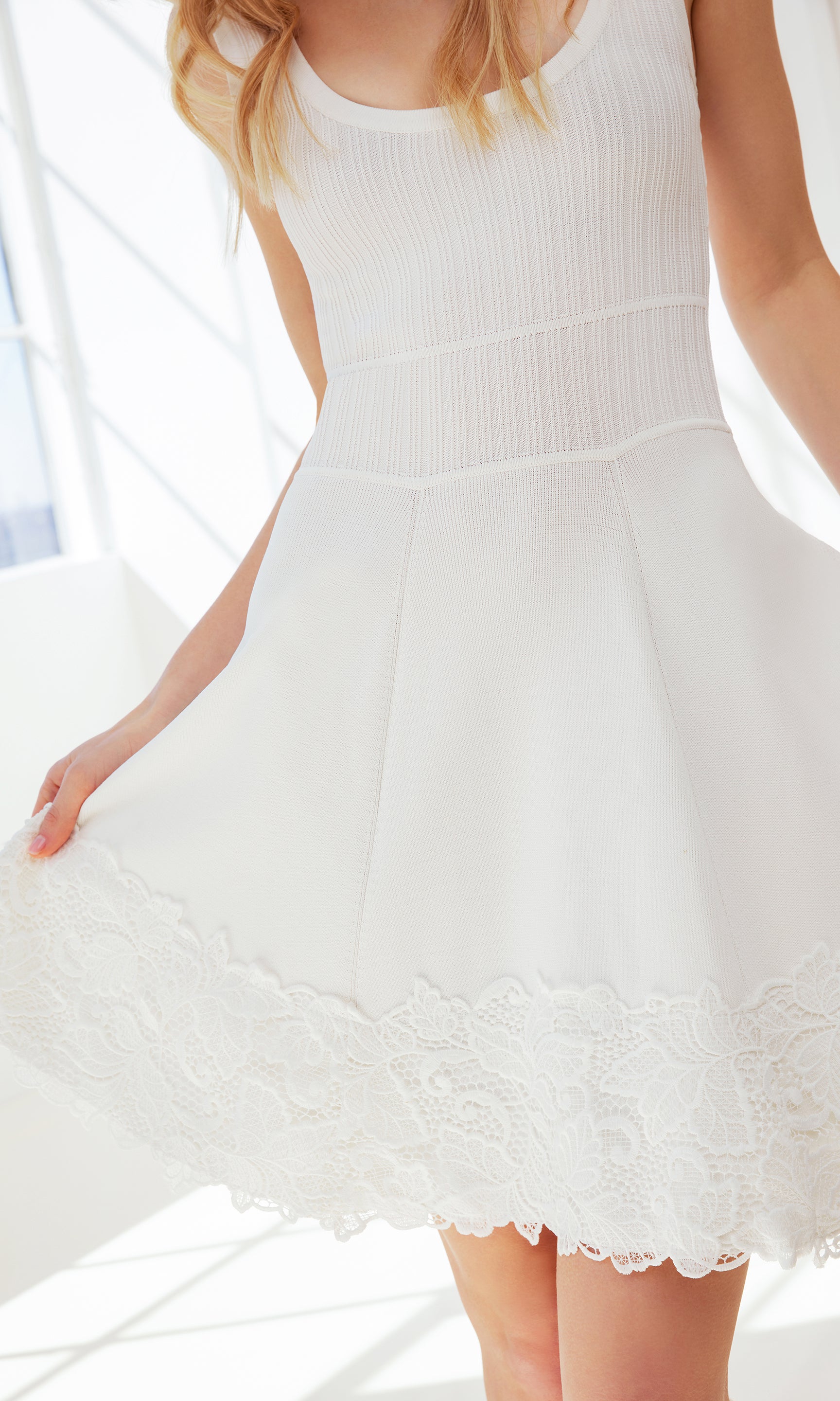zoomed in image of model posing in front of a window, wearing the Orpheus dress in white showcasing the floral design at the hem