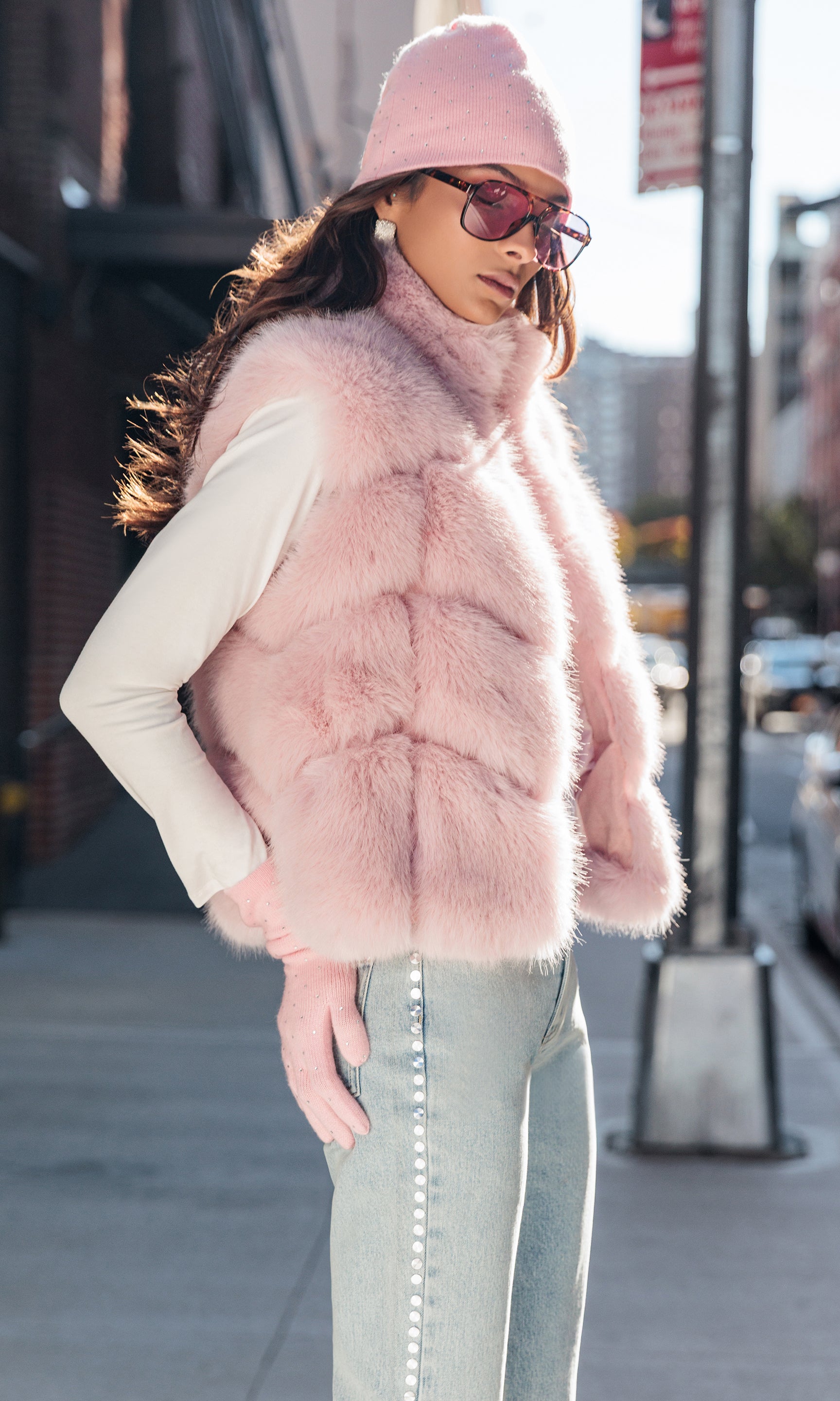 Woman wearing a pink fur vest and hat on a city street.
