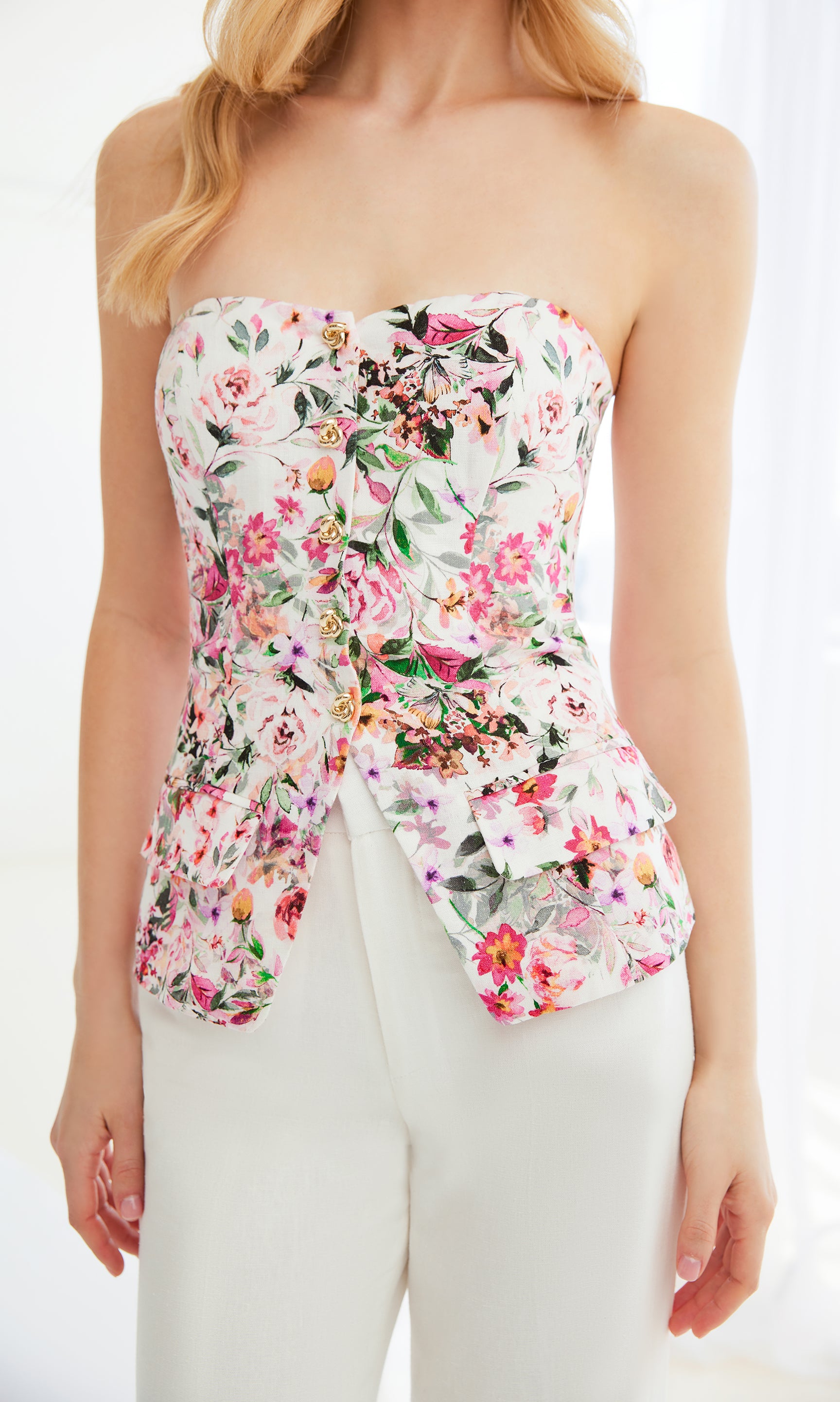 zoomed in image of model wearing the Quinn white vestier with a pink floral design, showcasing the delicate floral design paired with white trousers
