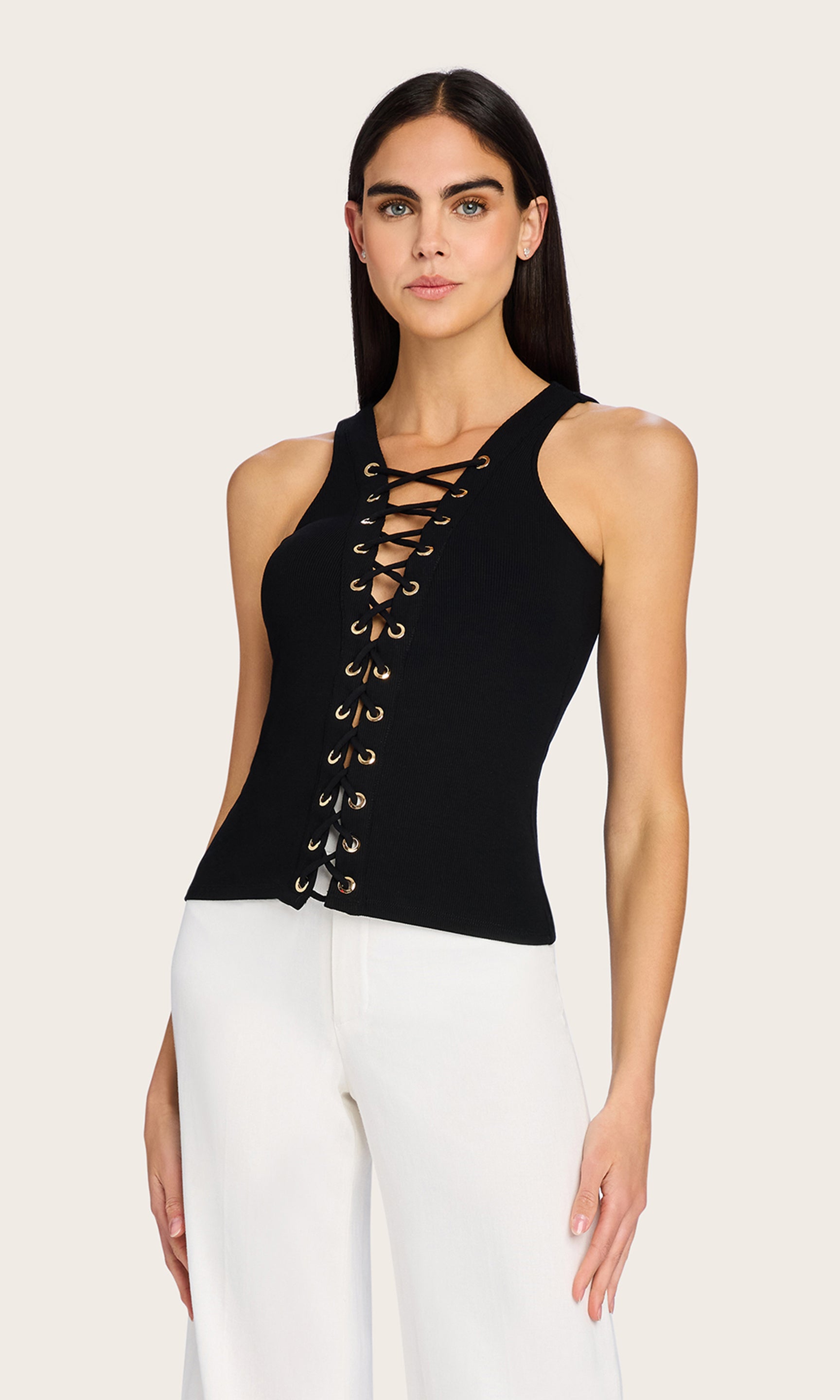 Front view image of model wearing the Rashelle Lace-Up Top in black, styled with white trousers to highlight the bold lace-up detail.