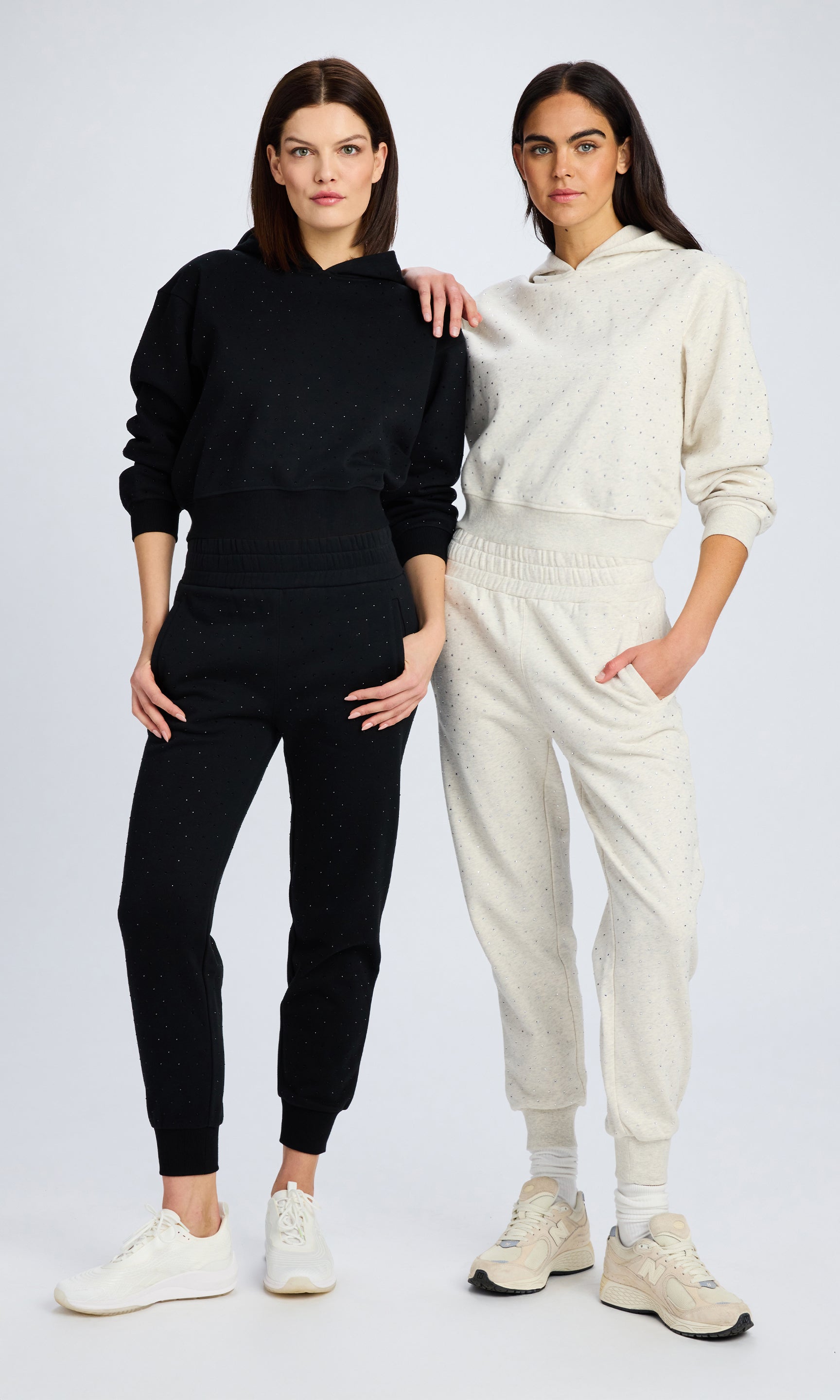 two models stand with each other. One model wears a matching black sweatsuit with crystals and the other wears a heather grey matching sweatsuit with crystals.