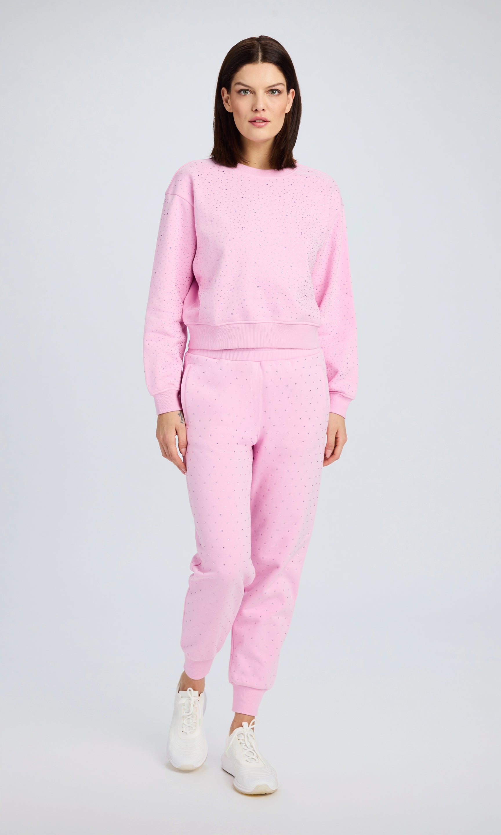 Model stands wearing a pink crystal embellished sweatsuit and white sneakers.