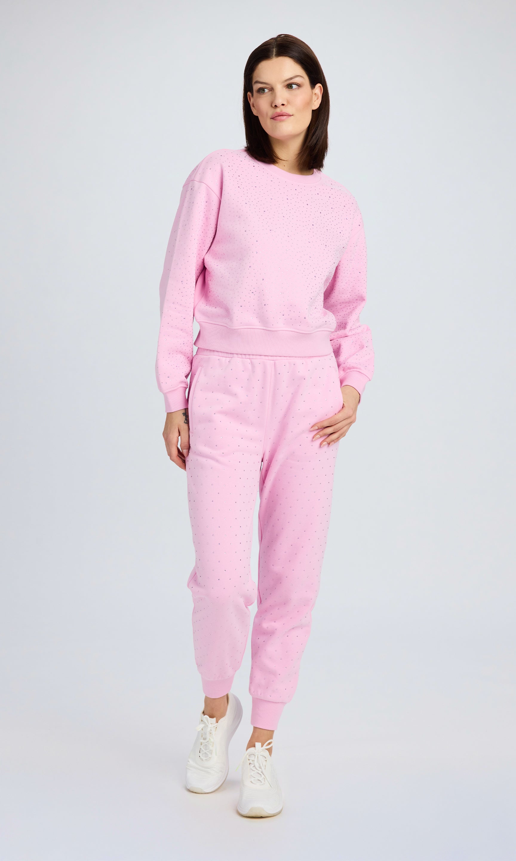 Model stands wearing a light pink sweatsuit with all over crystal detail