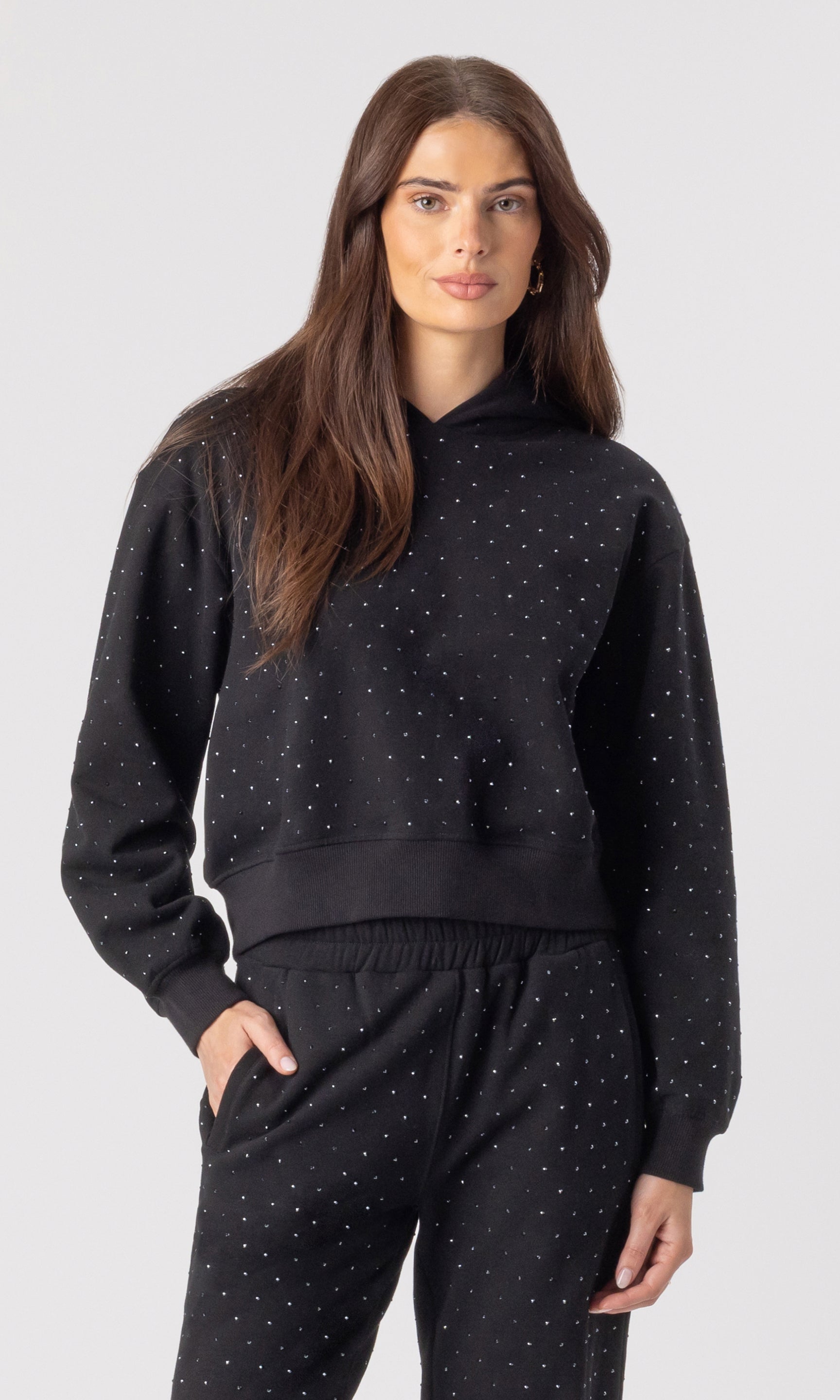 Woman wearing a black hoodie and pants with crystals on a white background