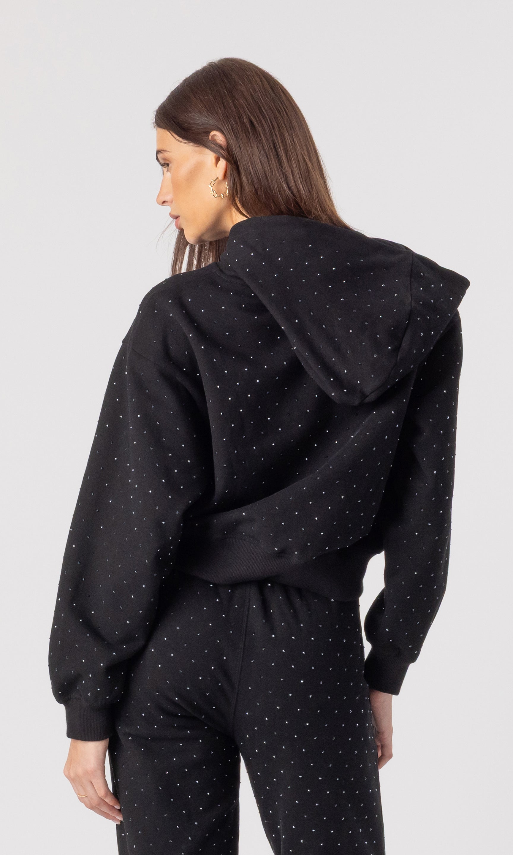Person wearing a black hoodie with crystals on a plain background