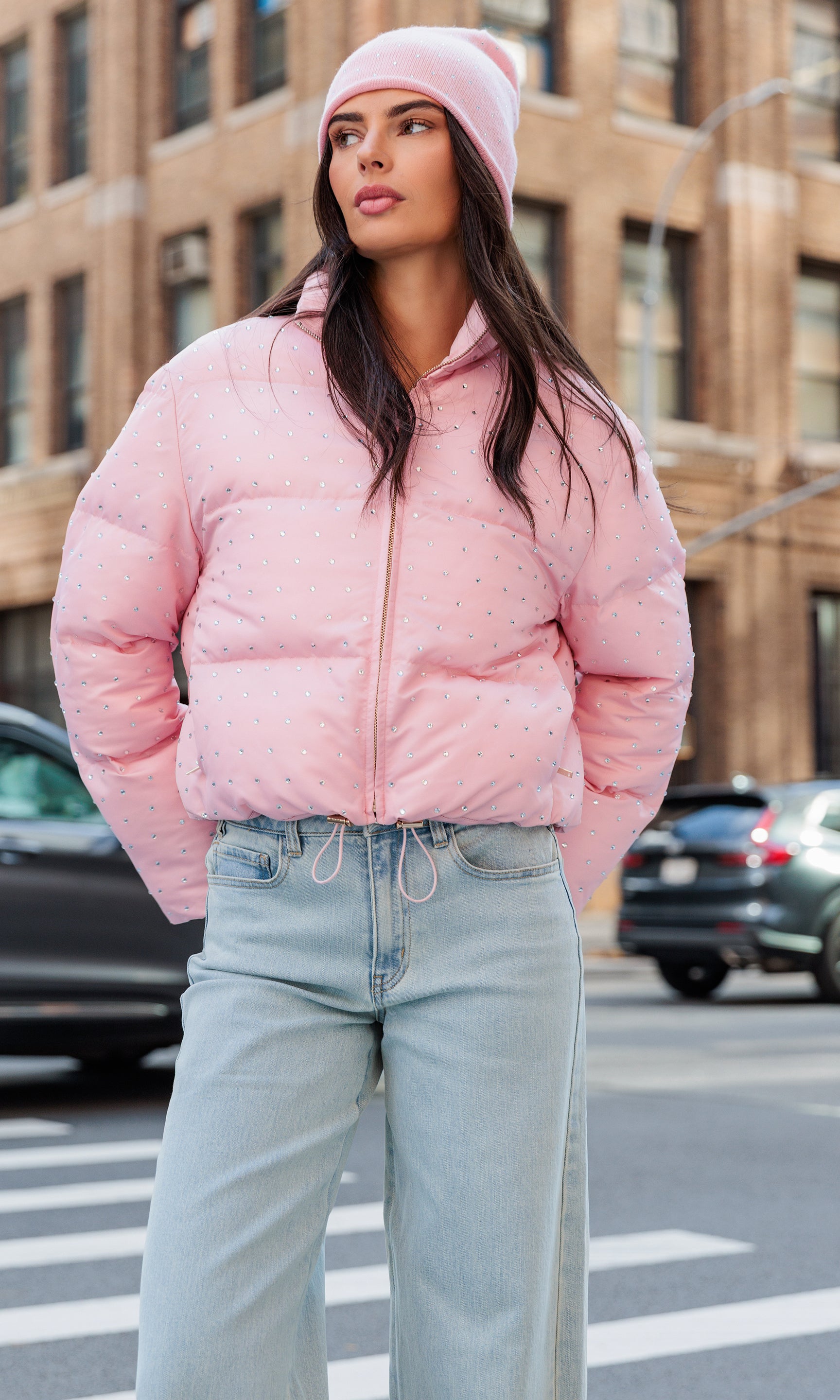 Woman wearing a pink puffer jacket and light blue jeans on a city street.
