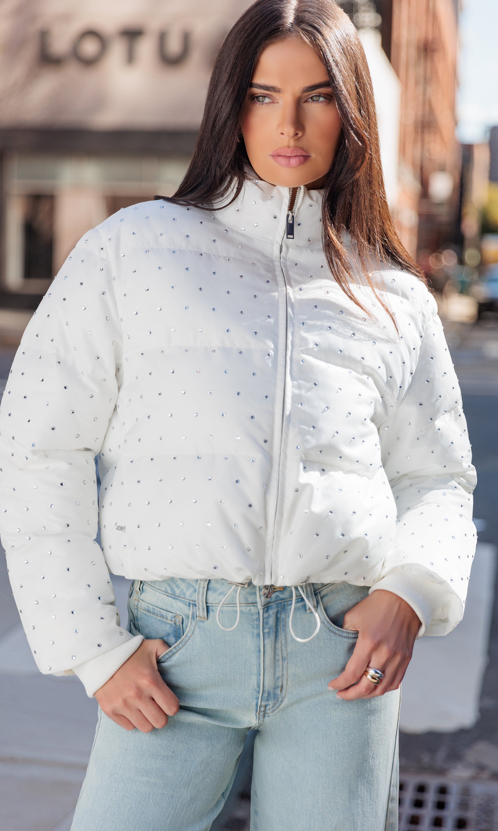 Woman wearing a white puffer jacket with crystal patterns outdoors.