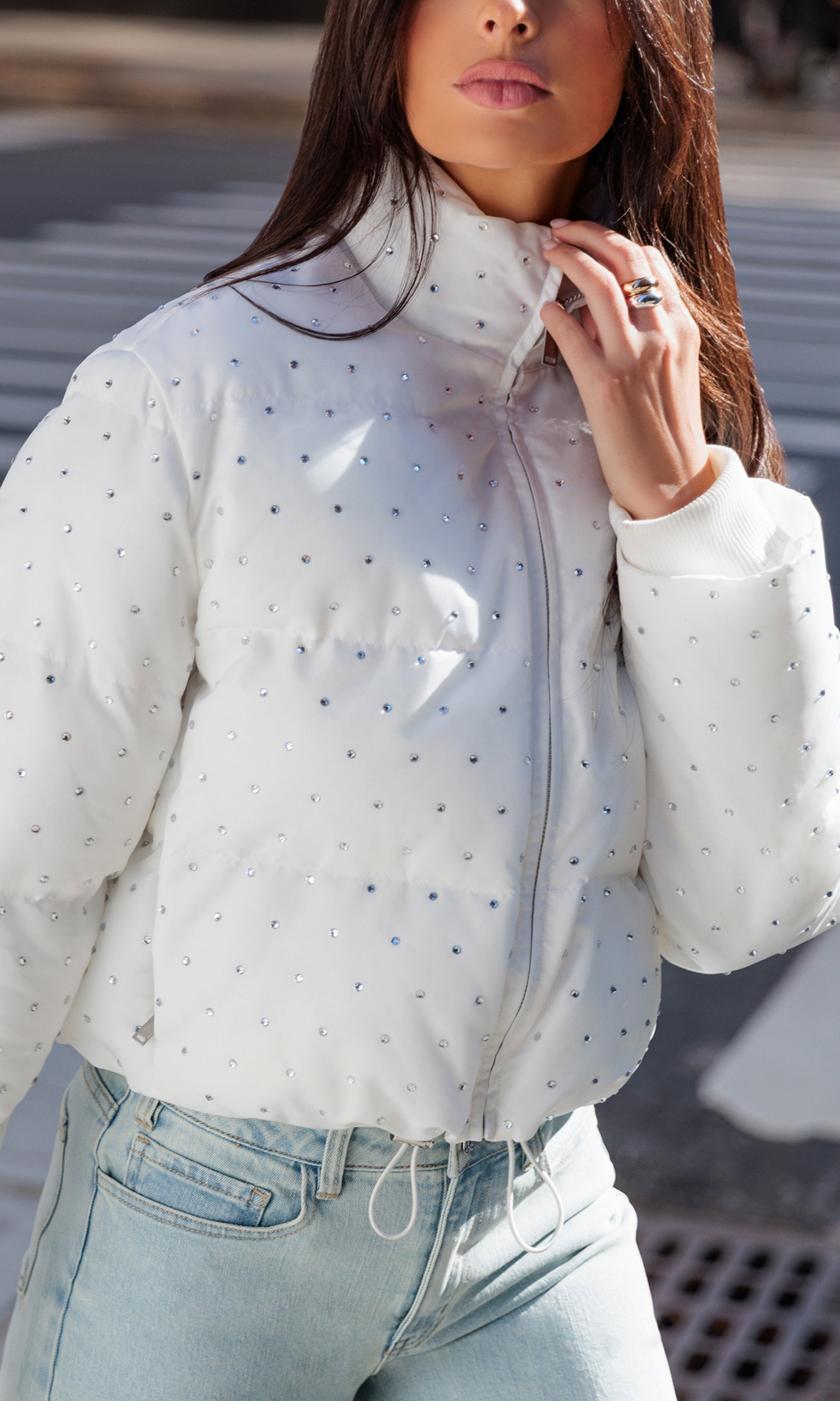 Person wearing a white puffer jacket with crystal embellishments and light blue jeans.