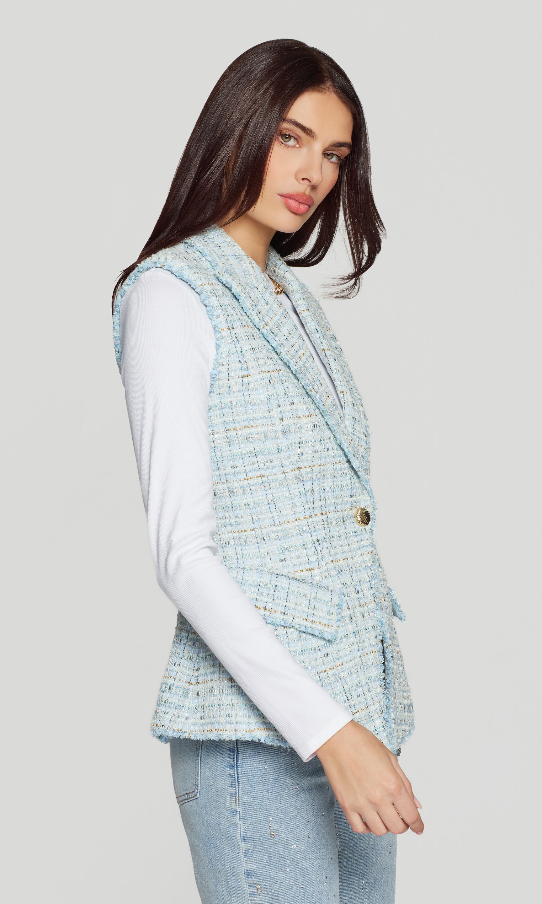 Side view of woman wearing a light blue tweed vest over a white shirt on a gray background