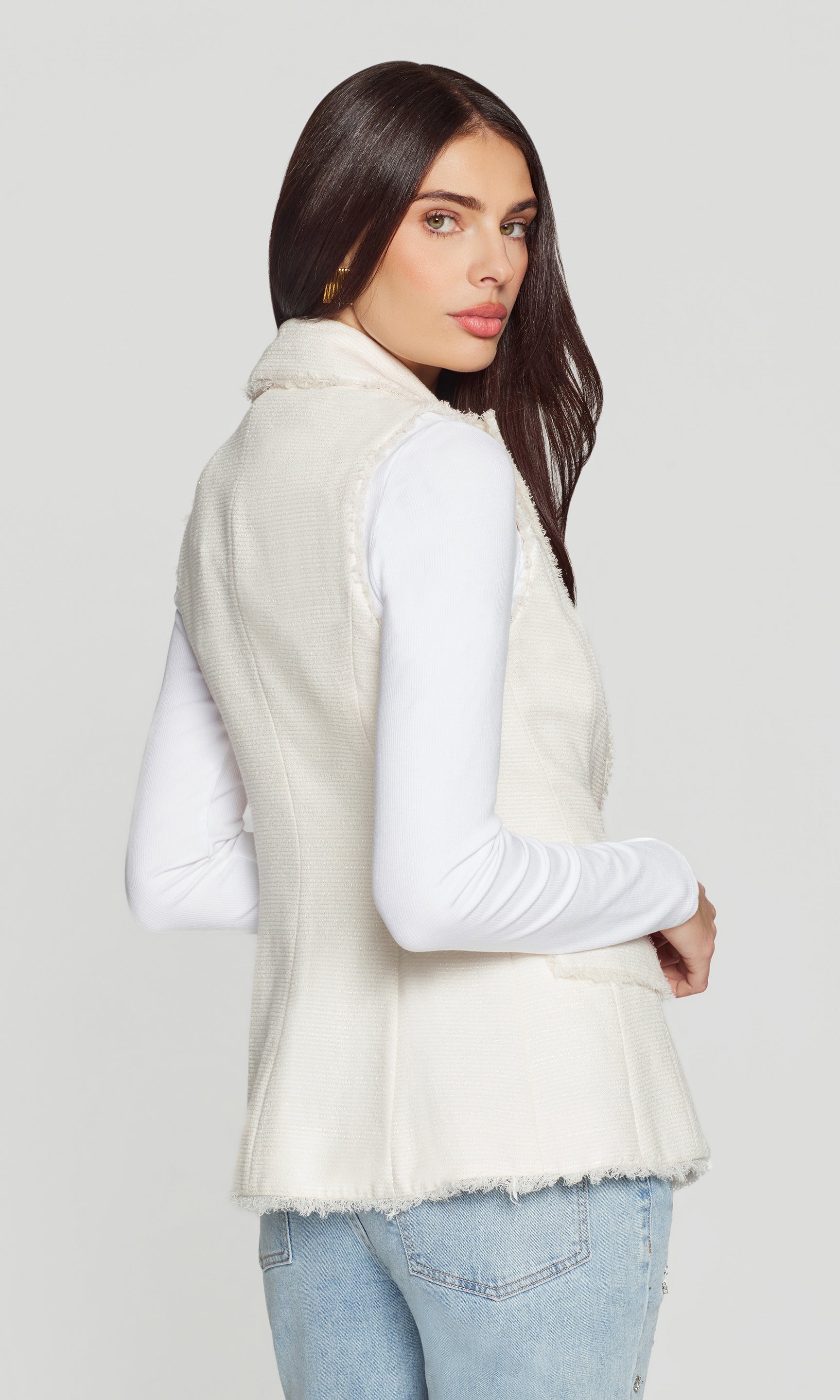 Woman wearing a cream-colored vest over a white shirt on a plain background