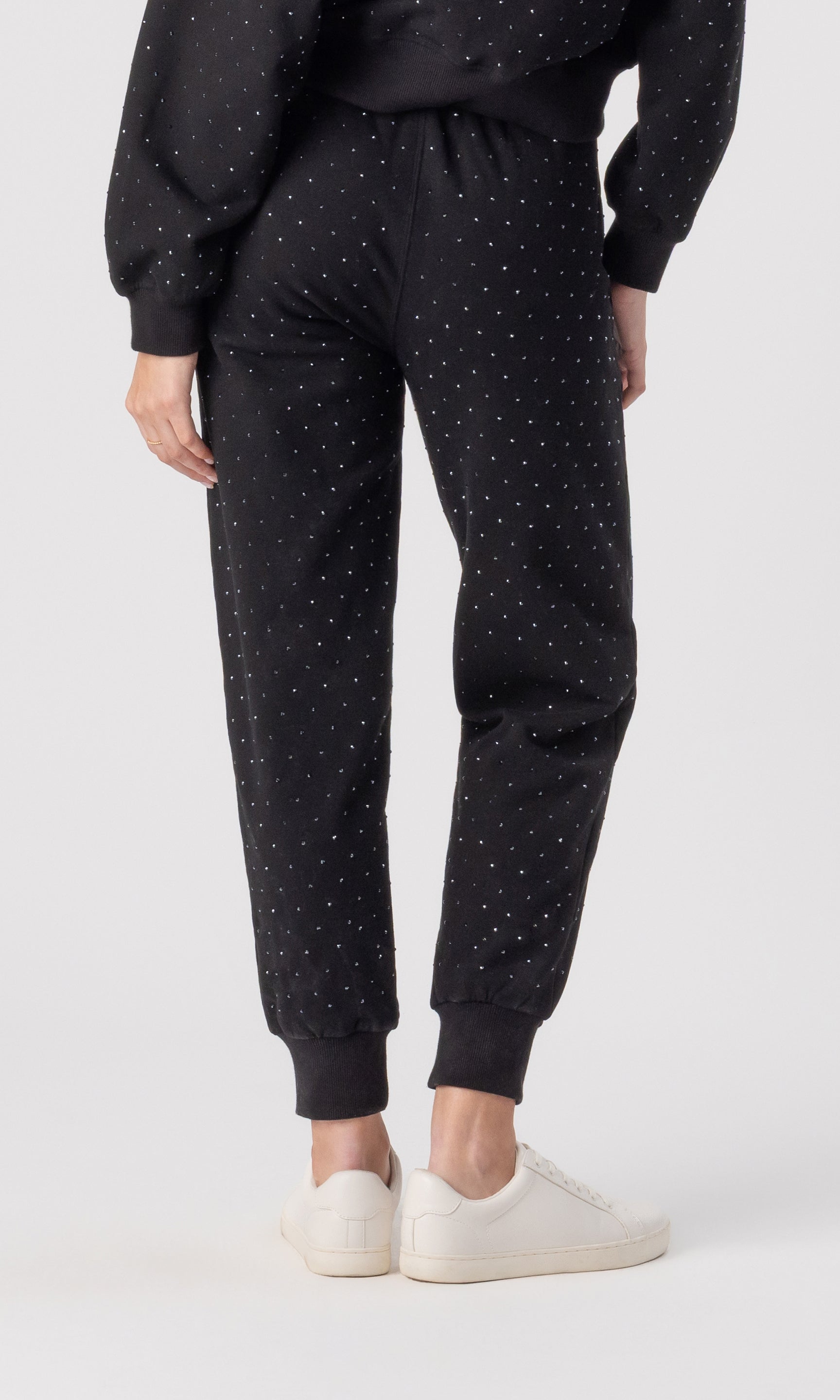 Person wearing black crystal pants and white sneakers on a white background
