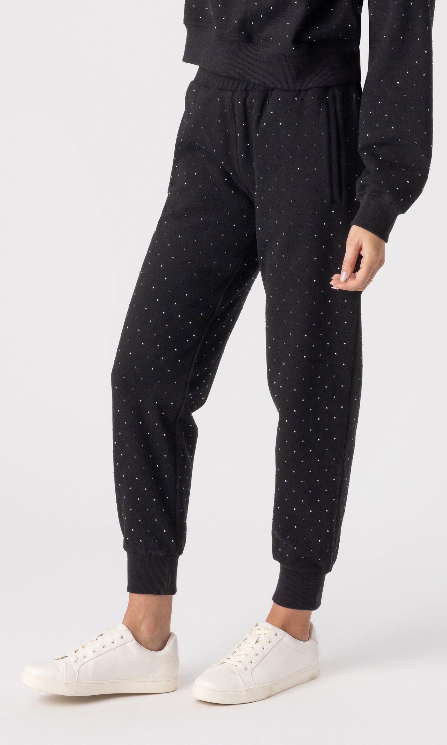Person wearing black crystal jogger pants and white sneakers on a white background