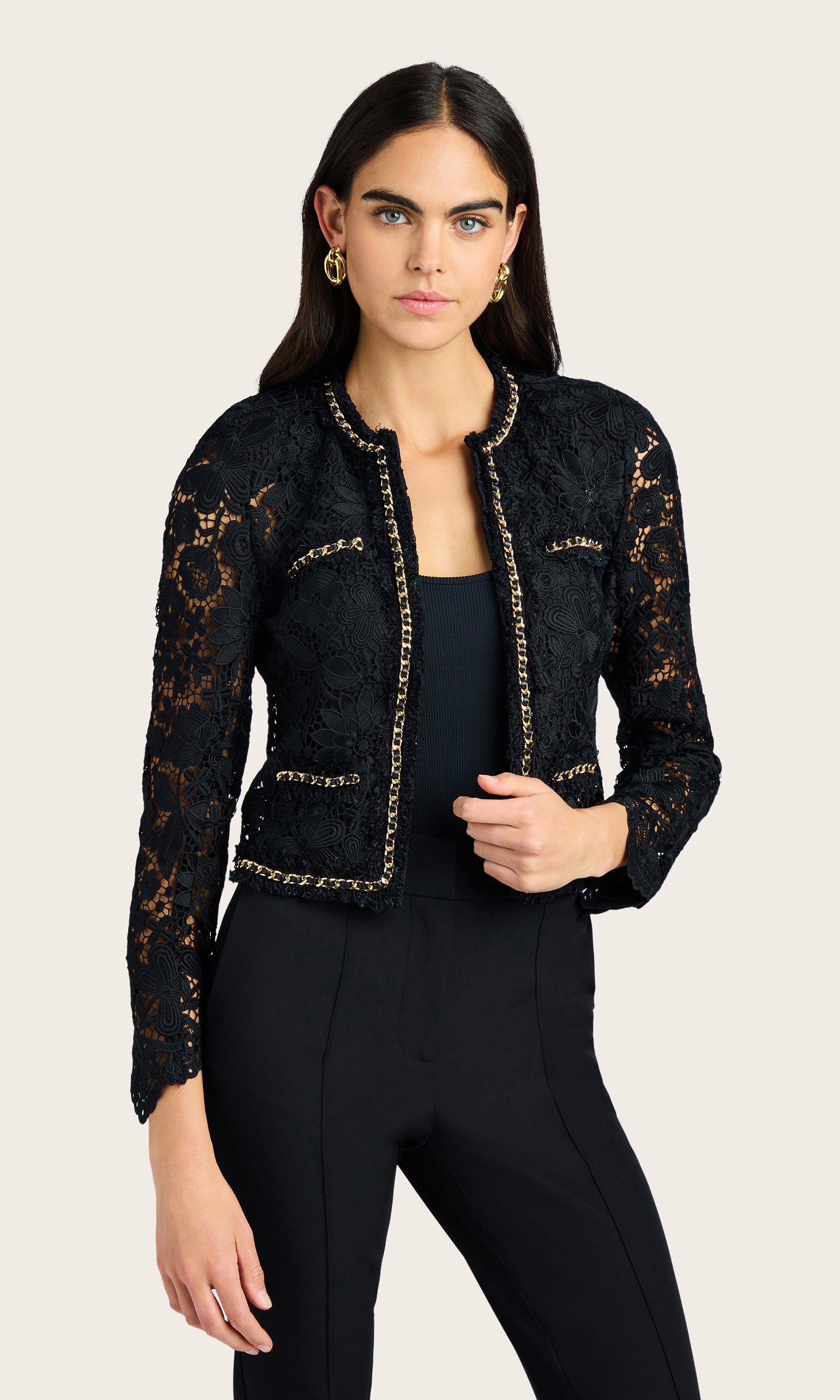 Front-facing studio view of the model in the black lace jacket with hands held together at the center
