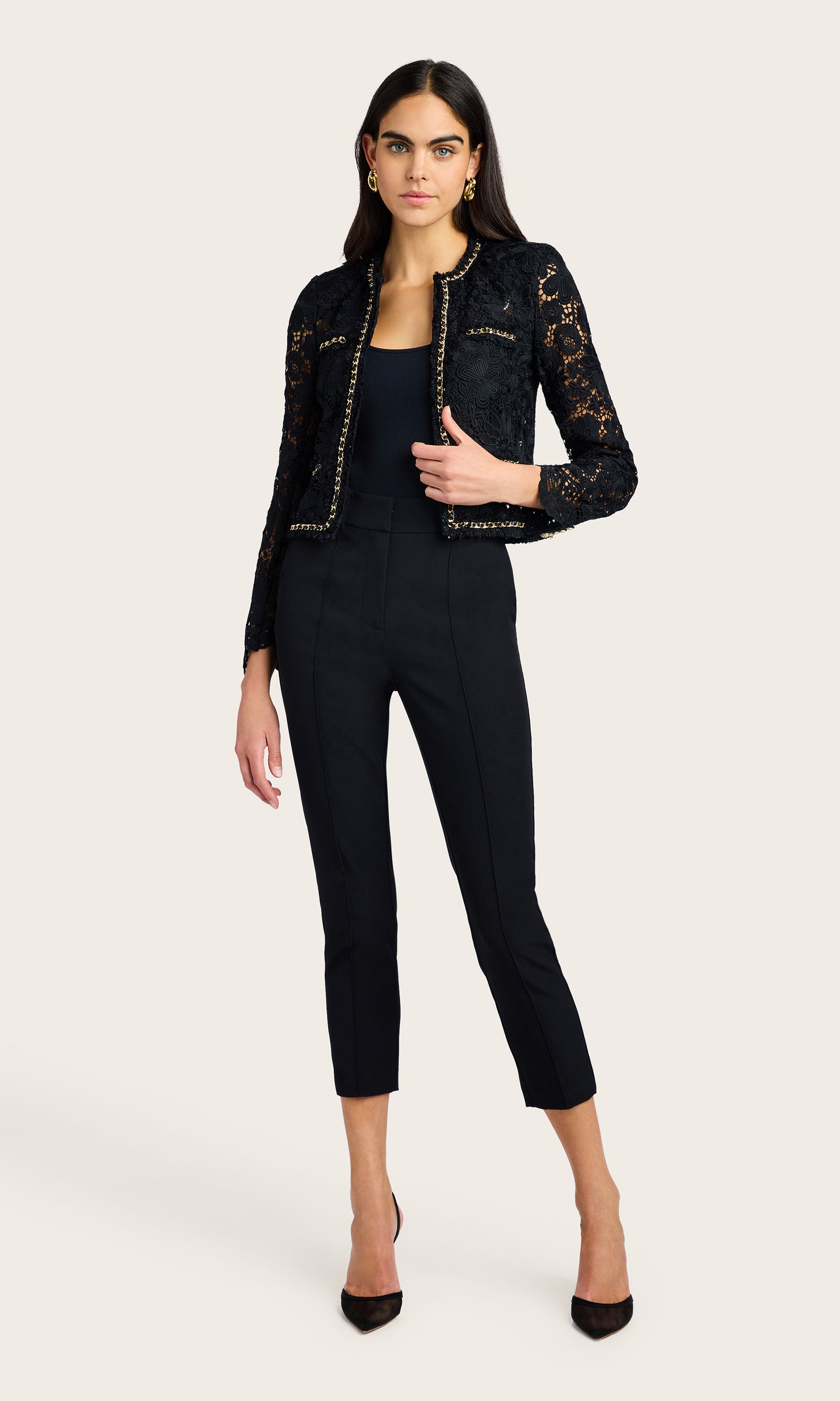Full-body studio shot of the model in the black lace jacket and slim pants standing in a relaxed pose