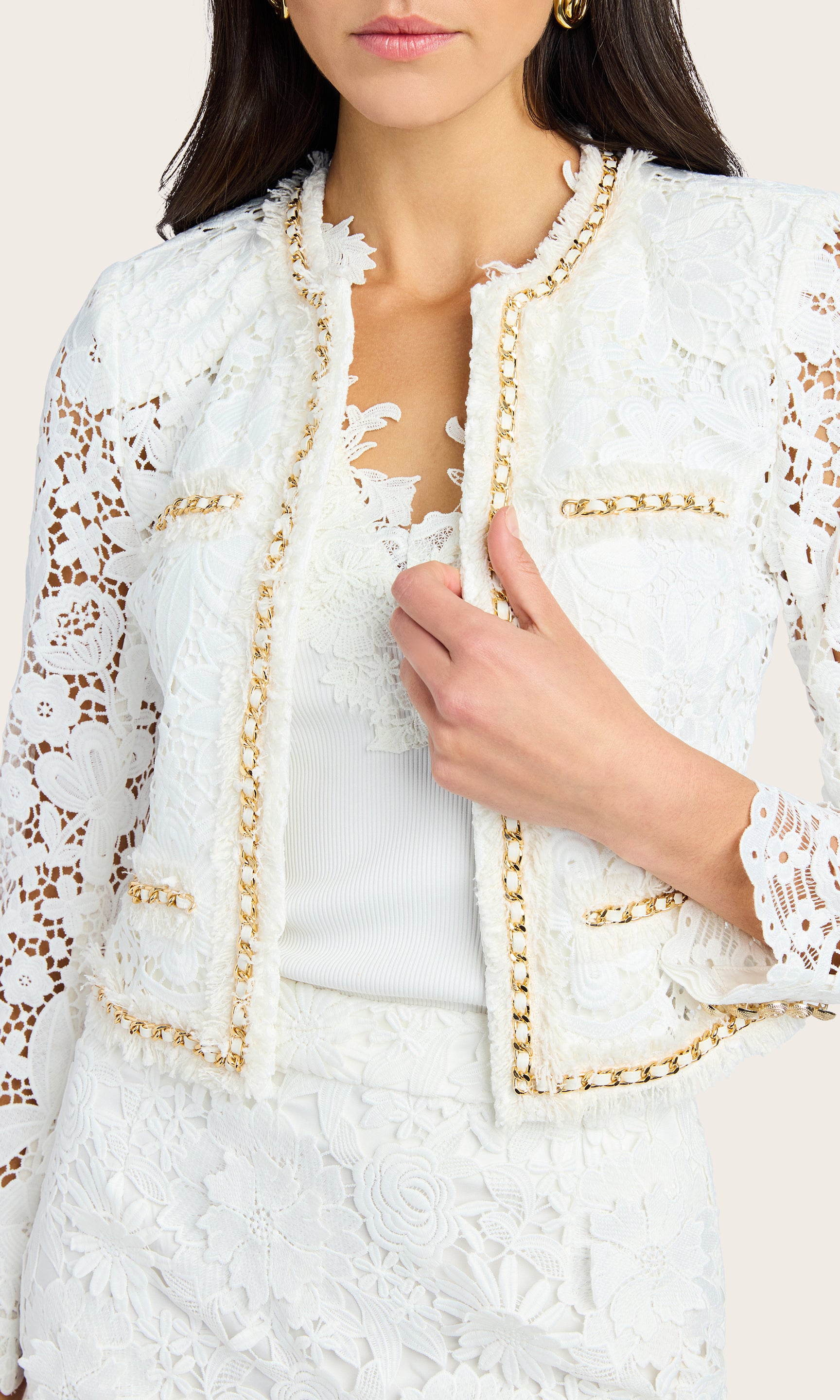 Close-up crop focusing on the lace detail and chain trim of the white blazer