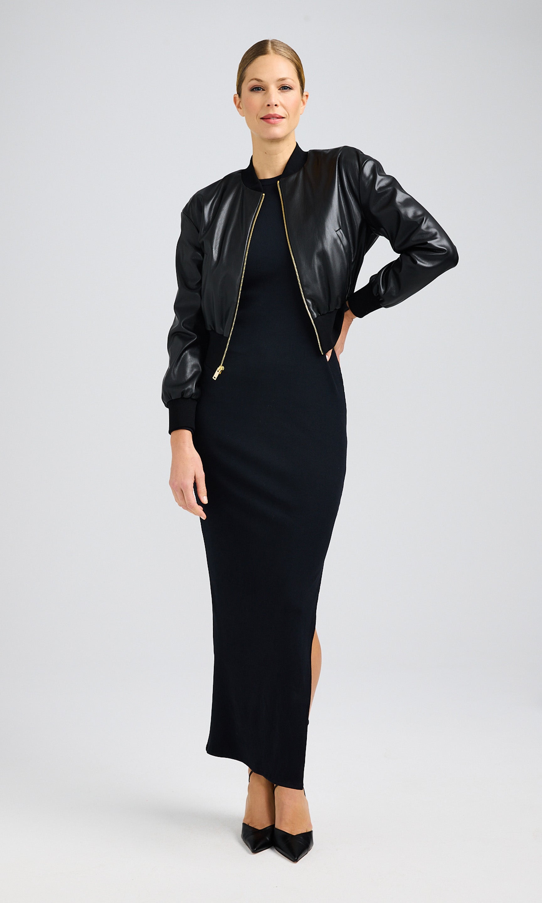 Woman wearing a black vegan leather bomber jacket with a black maxi dress and pointy black heels.