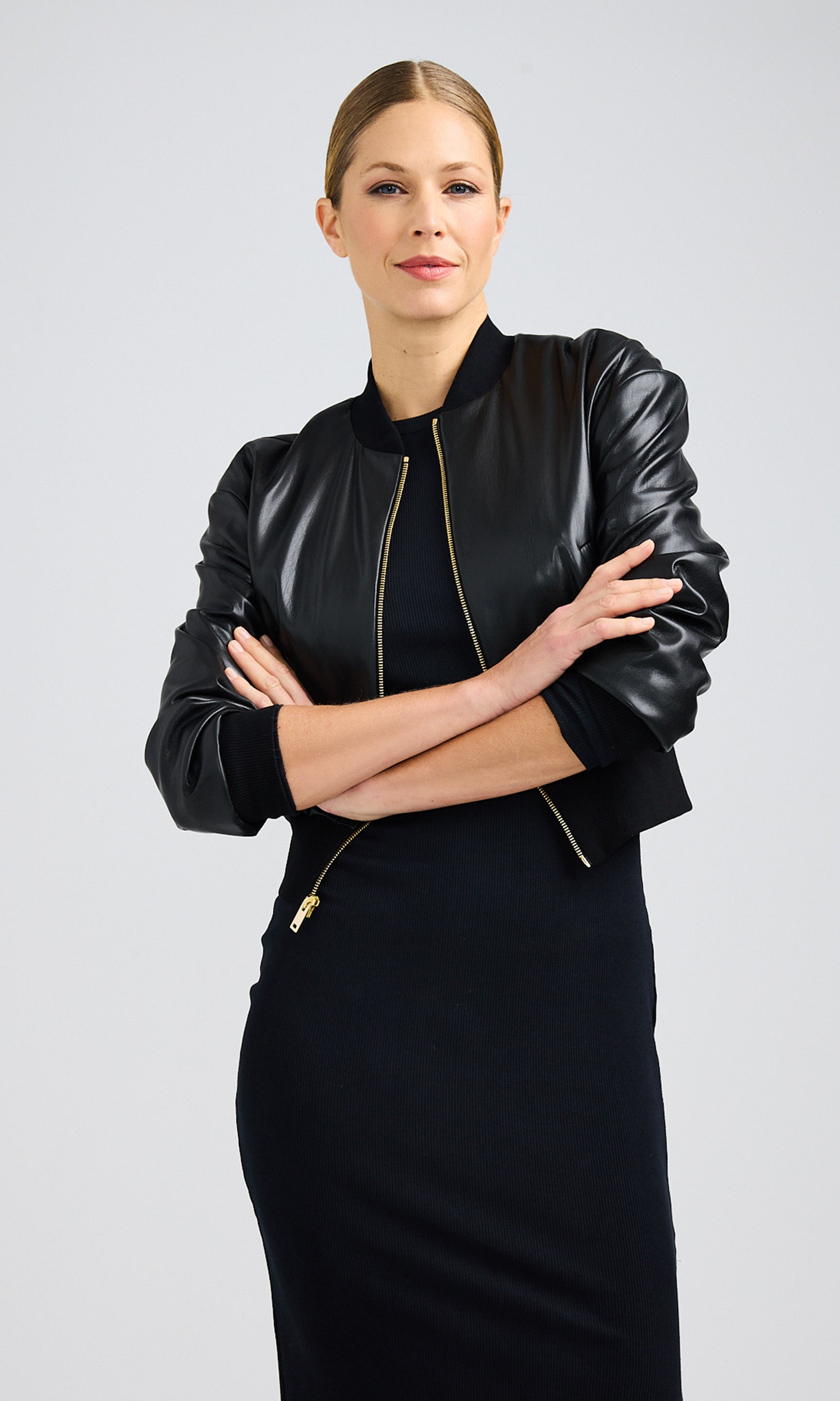 Woman crossing her arms in the front while wearing a black vegan leather bomber jacket over a dress.