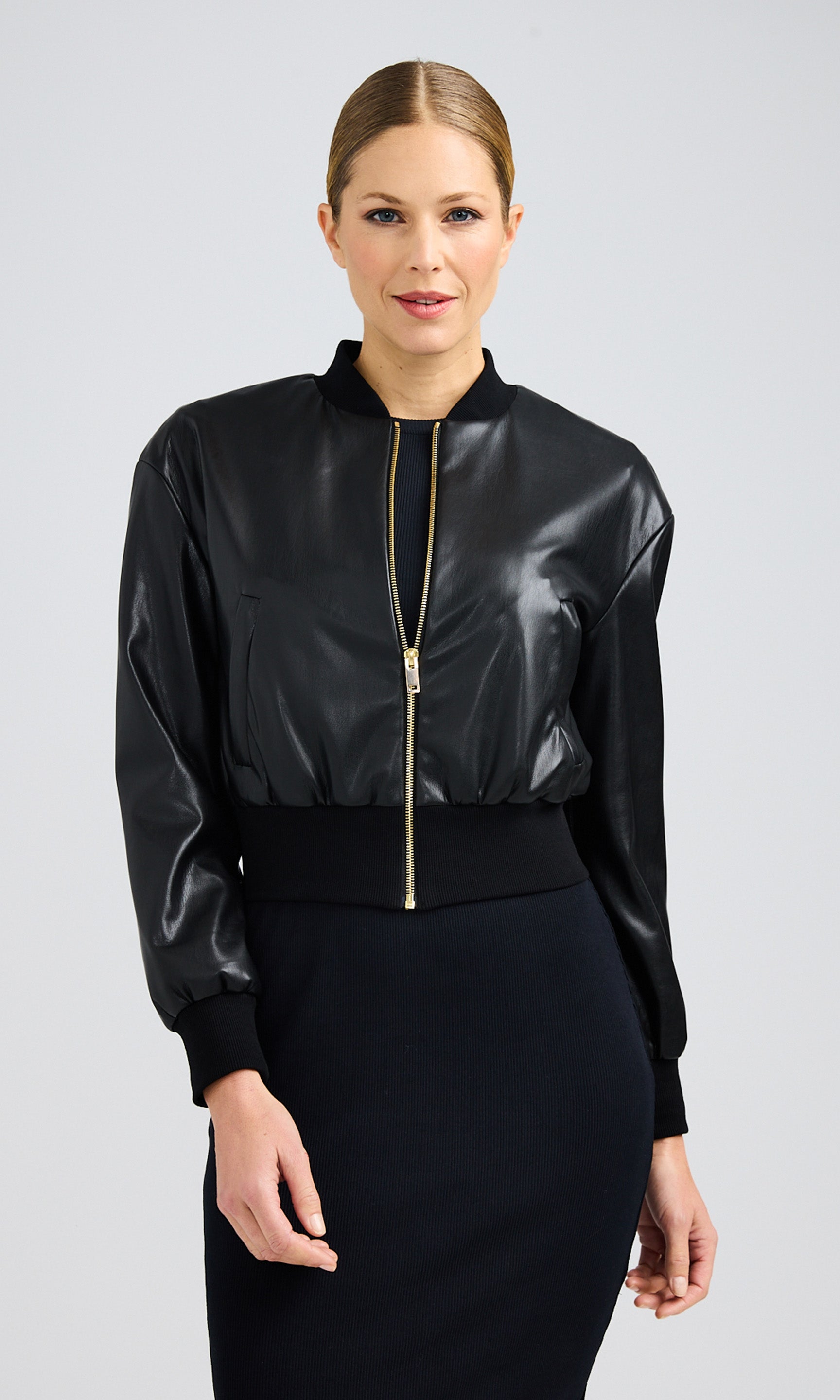 Woman wearing a zipped-up, black vegan leather bomber with a gold zipper paired with a black dress.