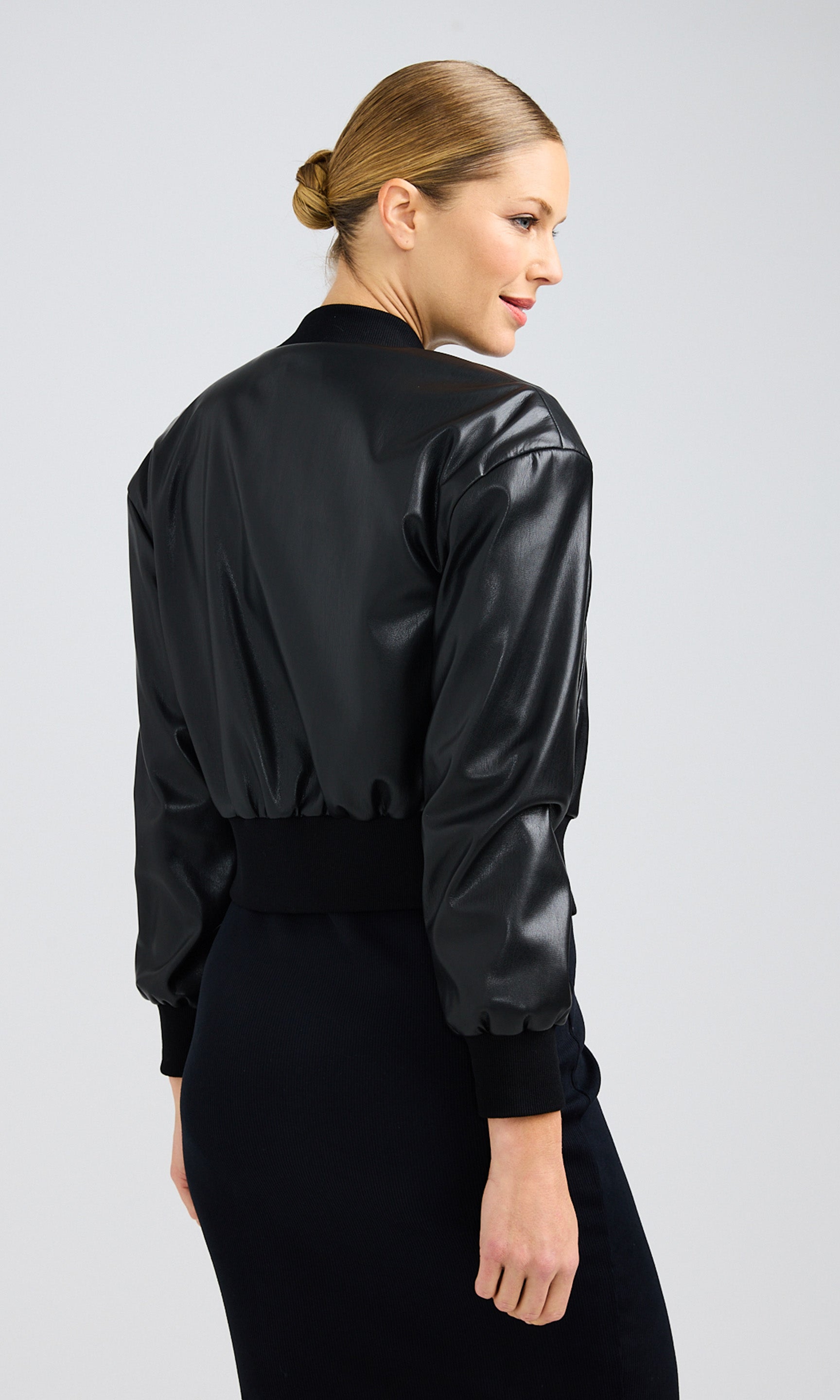 Rear-view of woman looking over her shoulder while wearing a black vegan leather bomber.