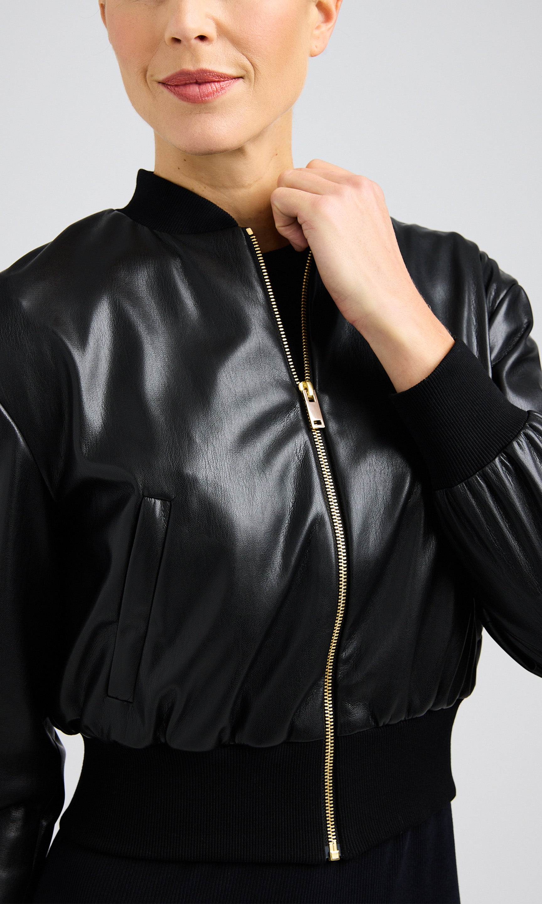 Close-up of woman wearing a zipped black bomber jacket made from vegan leather in a cropped length.