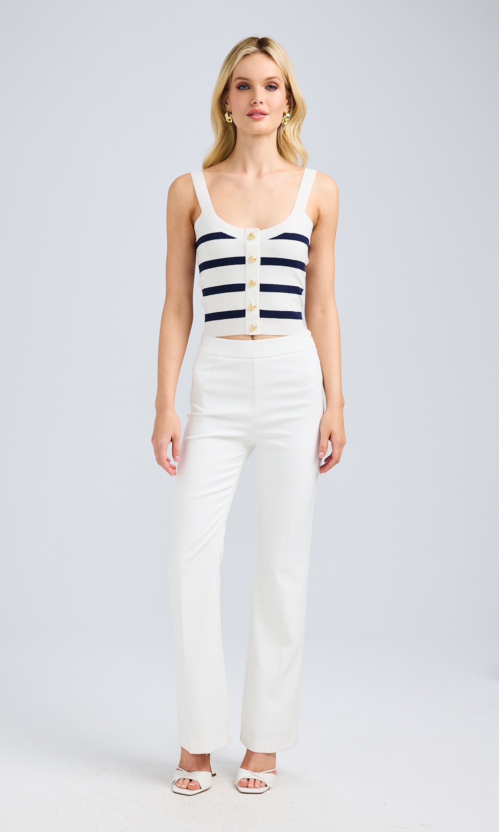 Full-body view of the model styling the striped knit bustier with tailored white pants for a chic look.