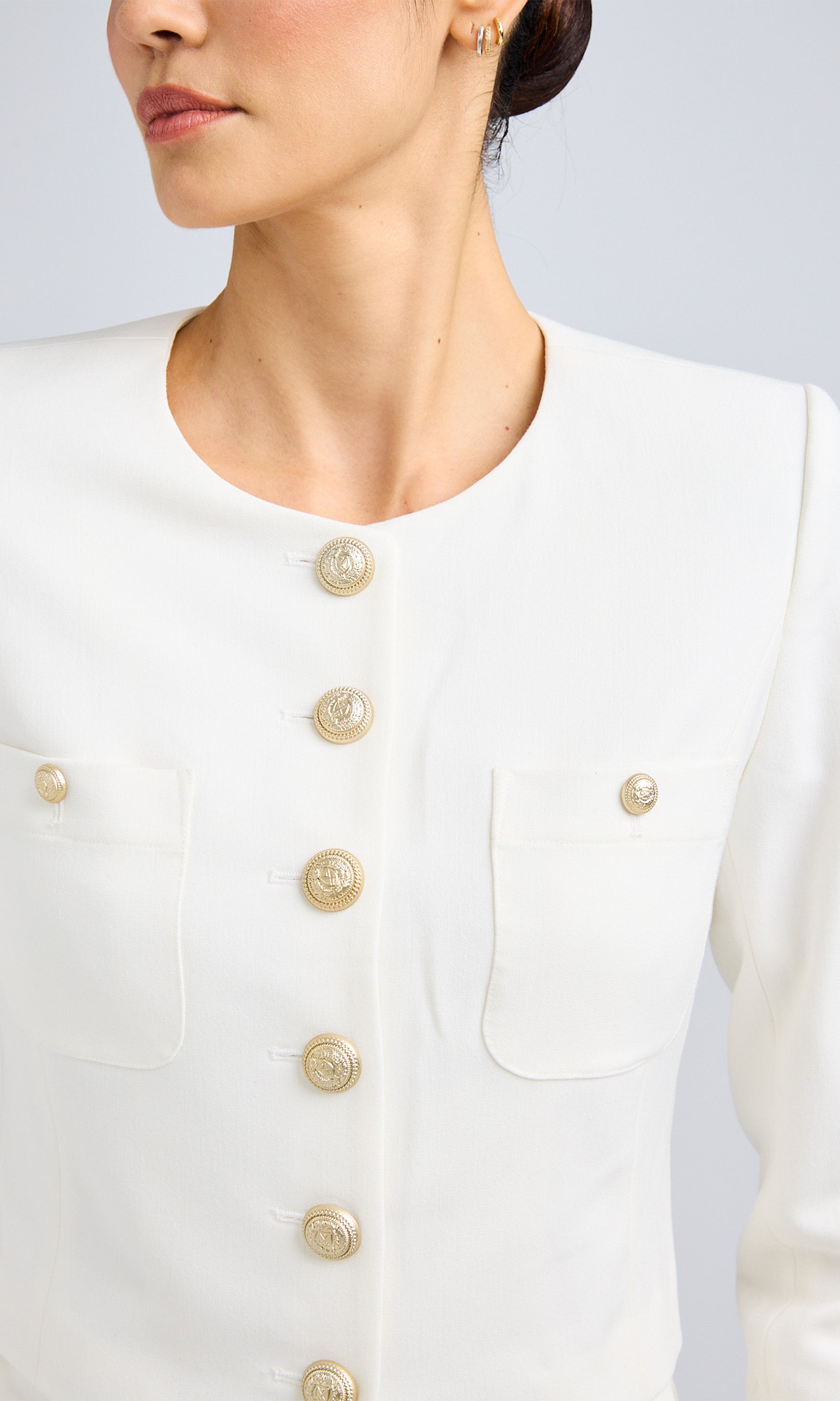 Close-up of a white structured jacket, showcasing gold button details and functional chest pockets.