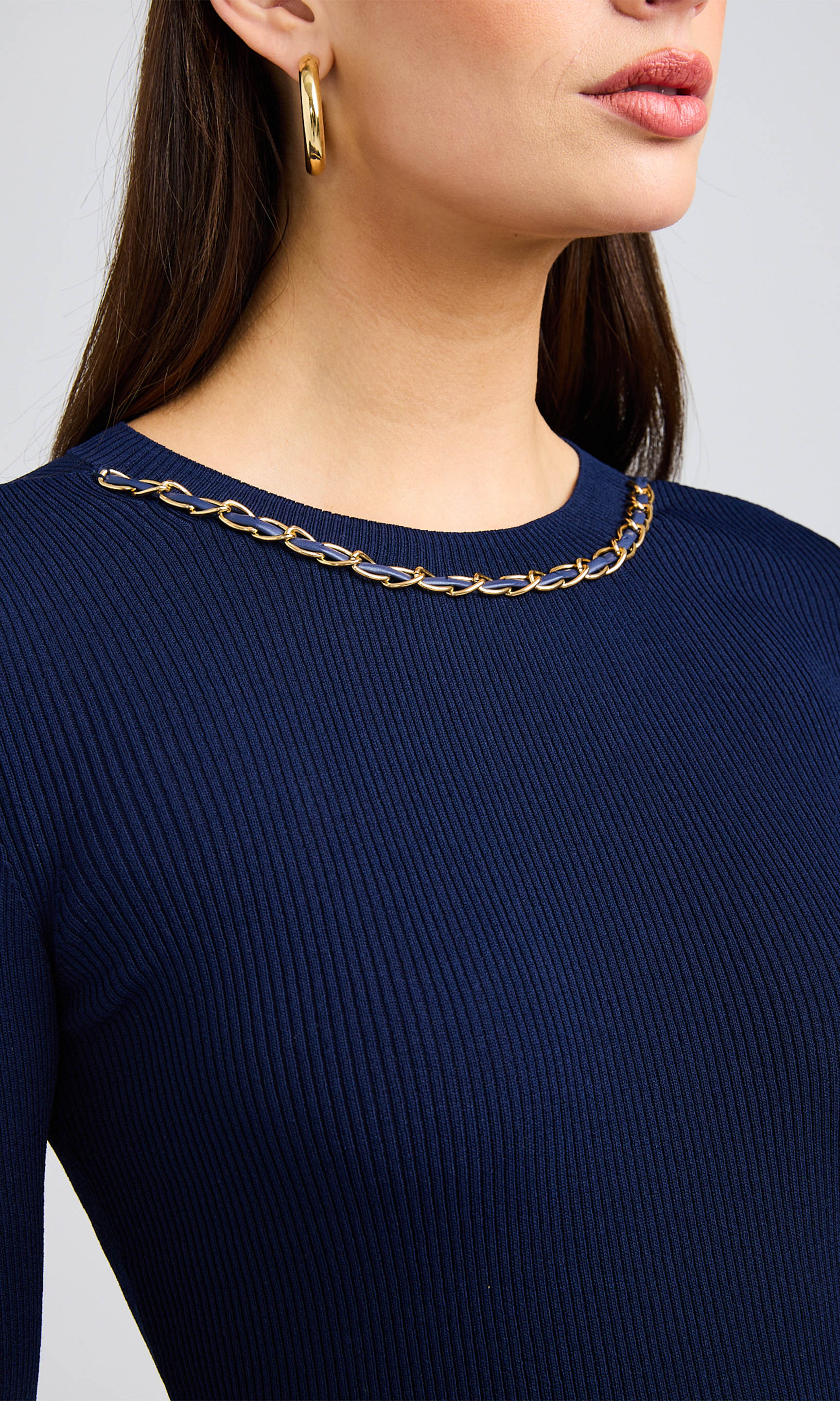 Close-up of woman wearing a navy blue ribbed sweater with a gold chain detail at the neckline.