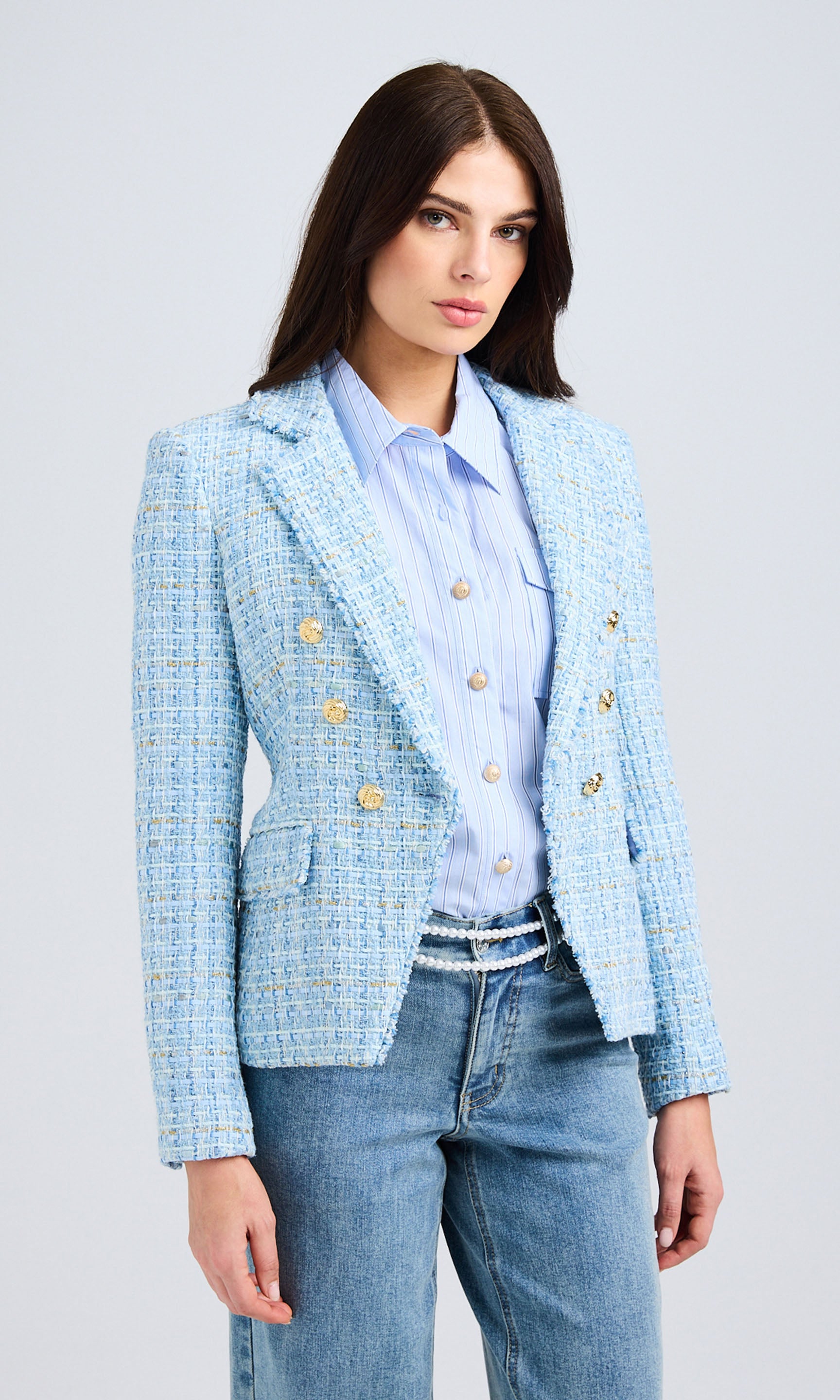 Front view of the model standing in a studio setting, wearing the blue tweed blazer with a buttoned-up look and paired with classic blue denim.