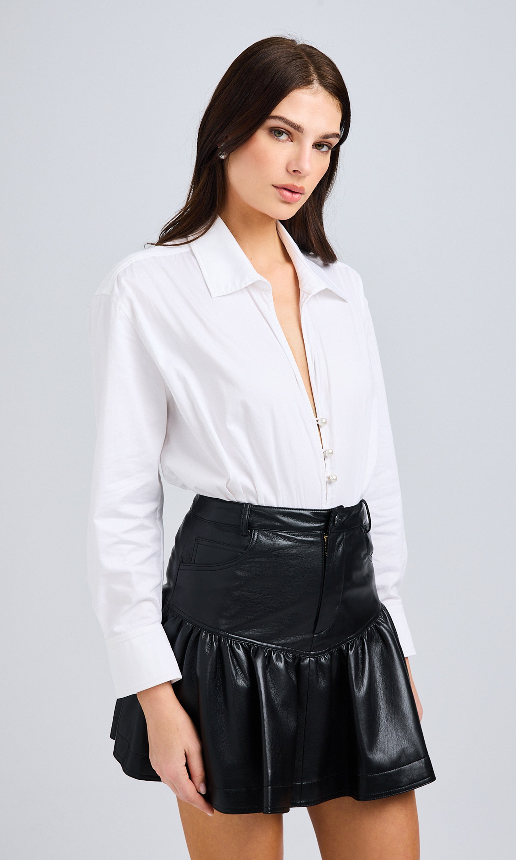 Front View Of Model Wearing A White Collared Bodysuit And Black Pleated Mini Skirt