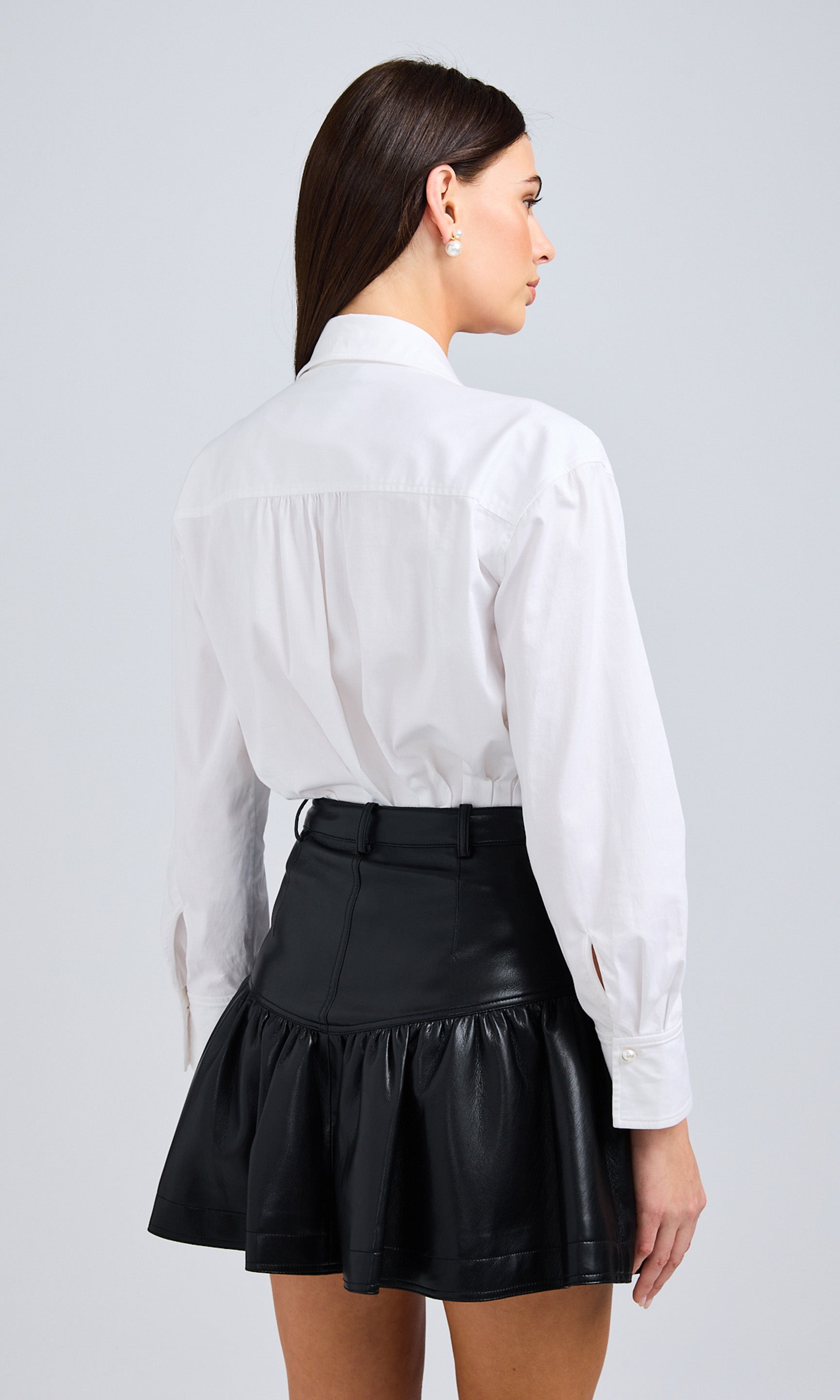 Rear View Of Model In A White Collared Bodysuit And Black Pleated Mini Skirt, Showcasing The Back Details