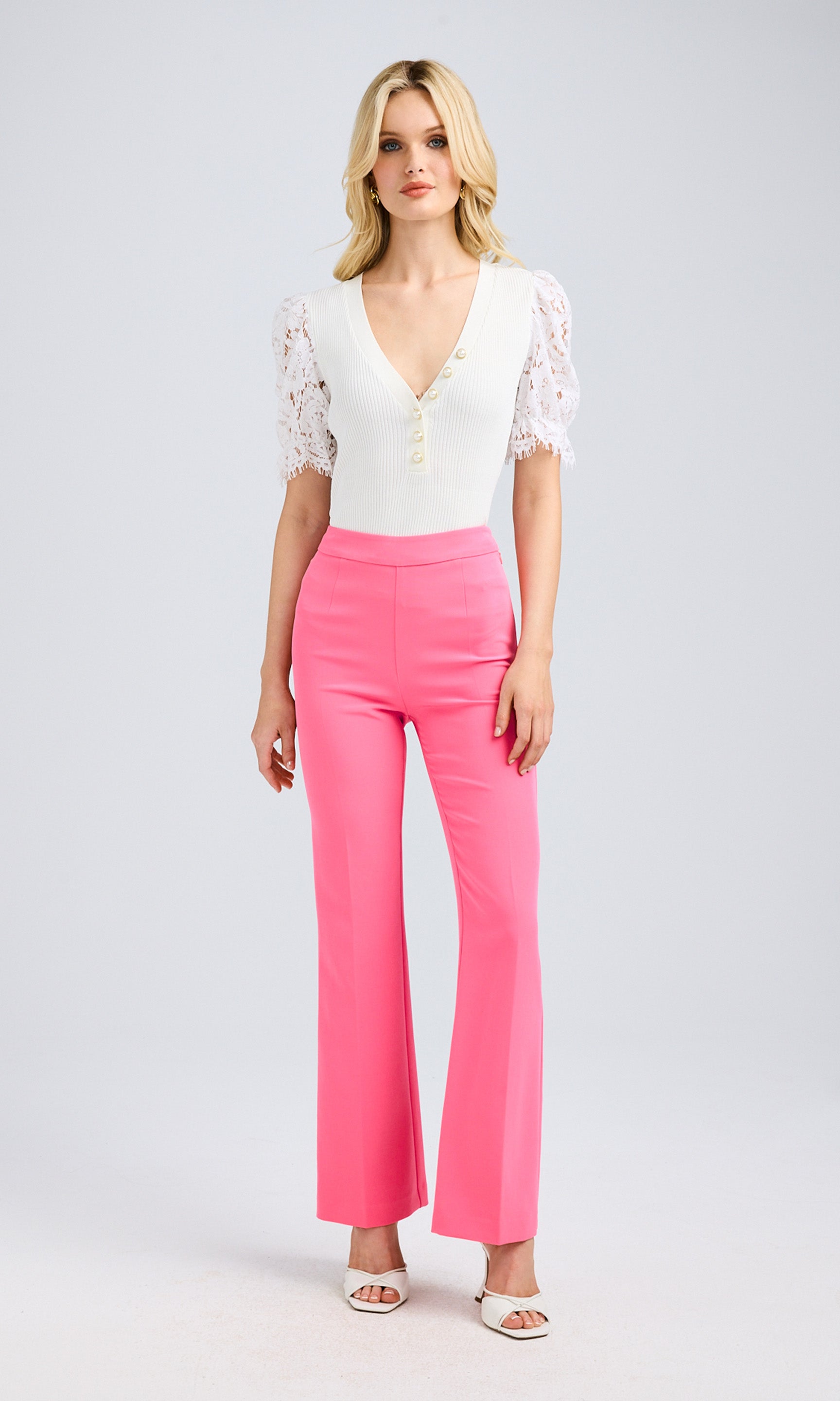 Full-body shot of the model wearing the white lace-sleeve top with high-waisted pink trousers.