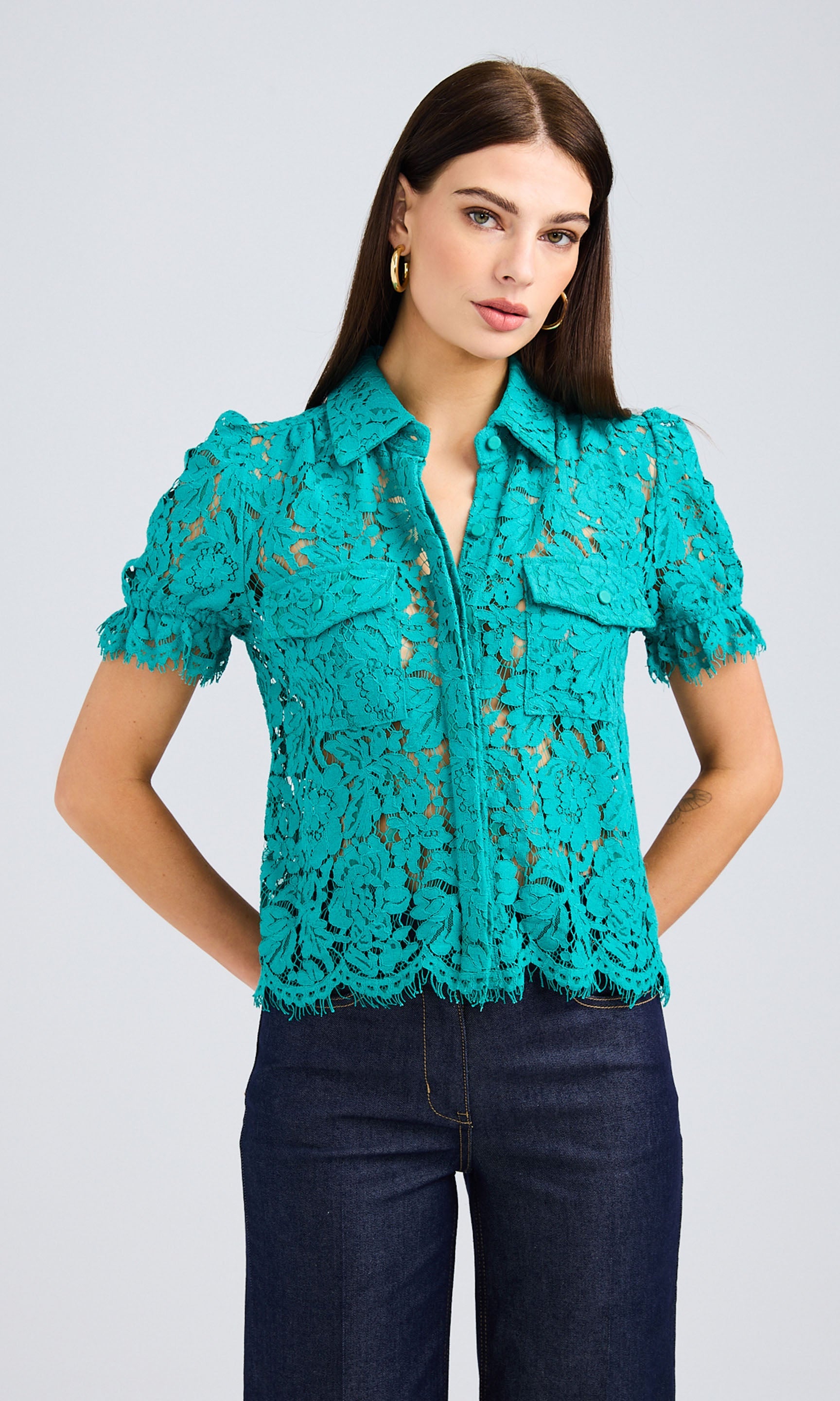 Dark-haired woman wearing a topaz lace button-up shirt with dark-wash denim jeans.