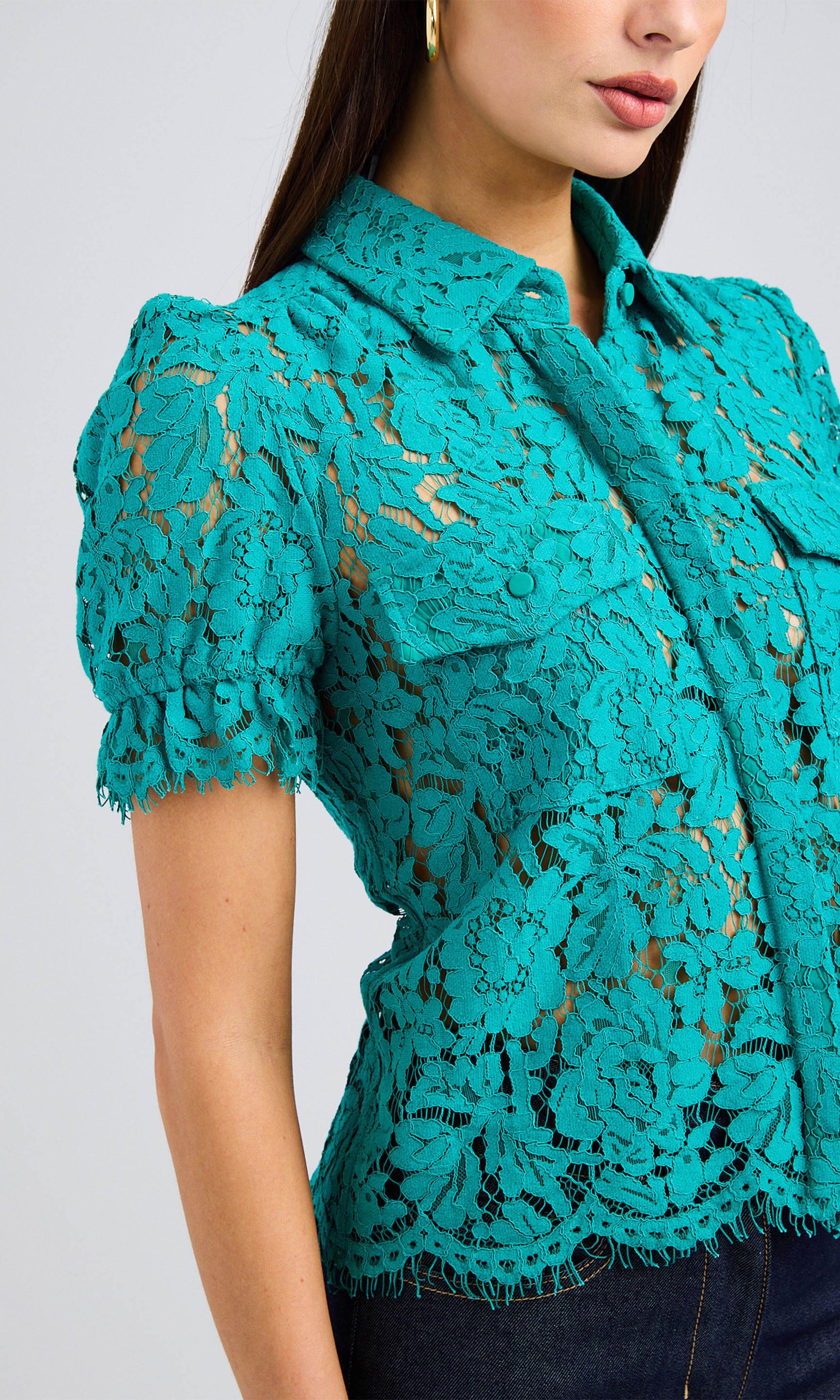 Close-up view of woman wearing a topaz-colored lace blouse with puff-sleeves and dark jeans.