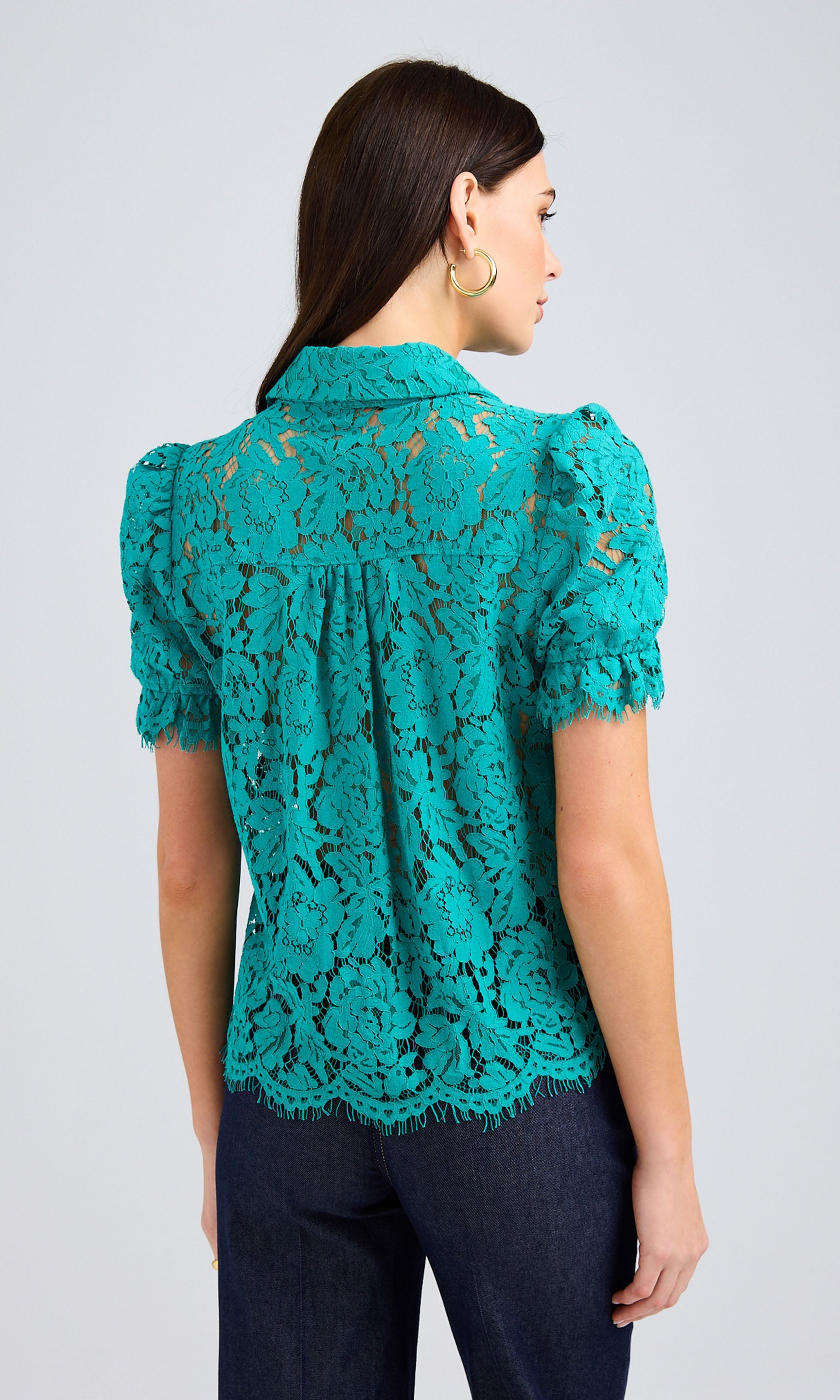 Rear view of woman wearing a topaz-colored lace blouse with short, puffed sleeves and dark jeans.