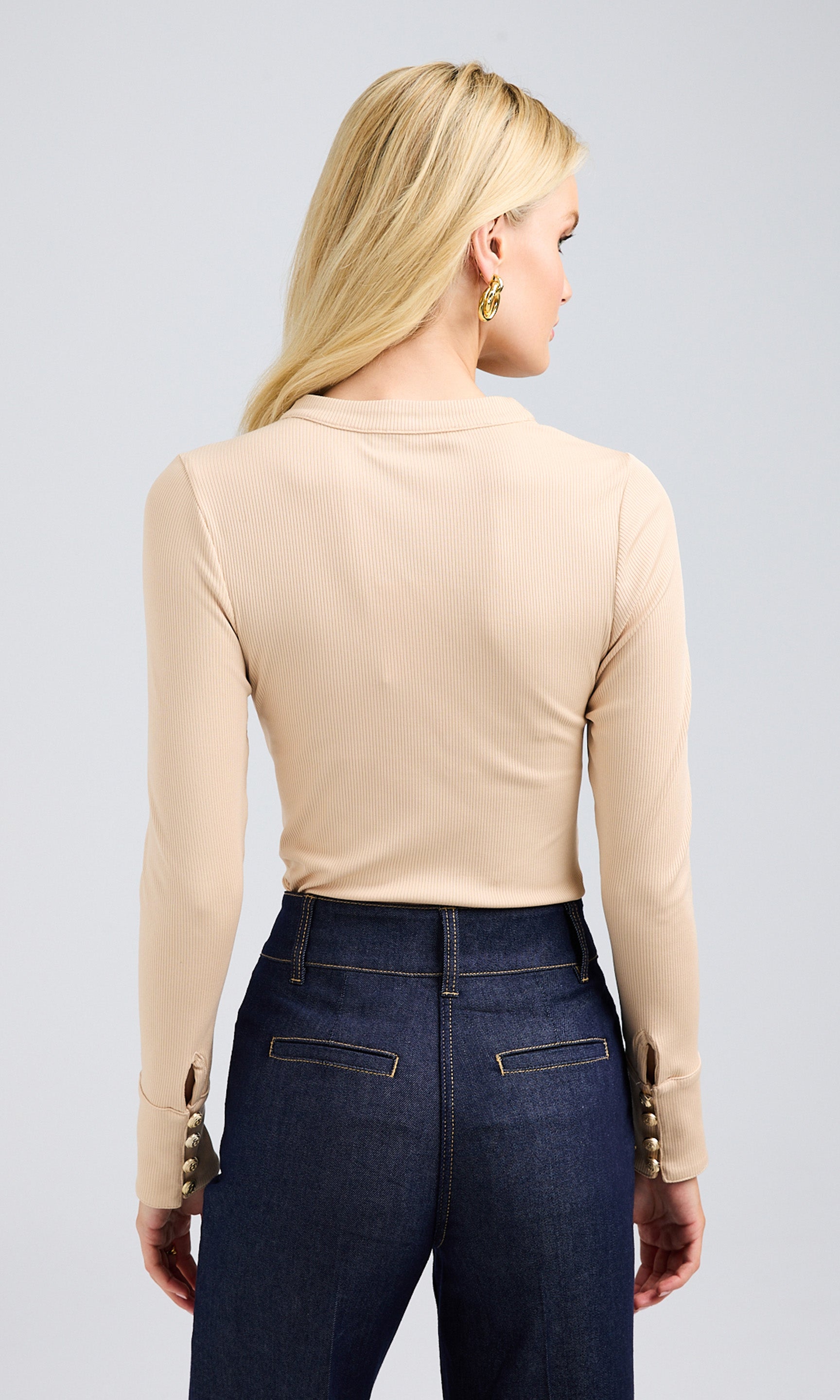 Rear view of sand-colored ribbed bodysuit, styled with dark-wash jeans.