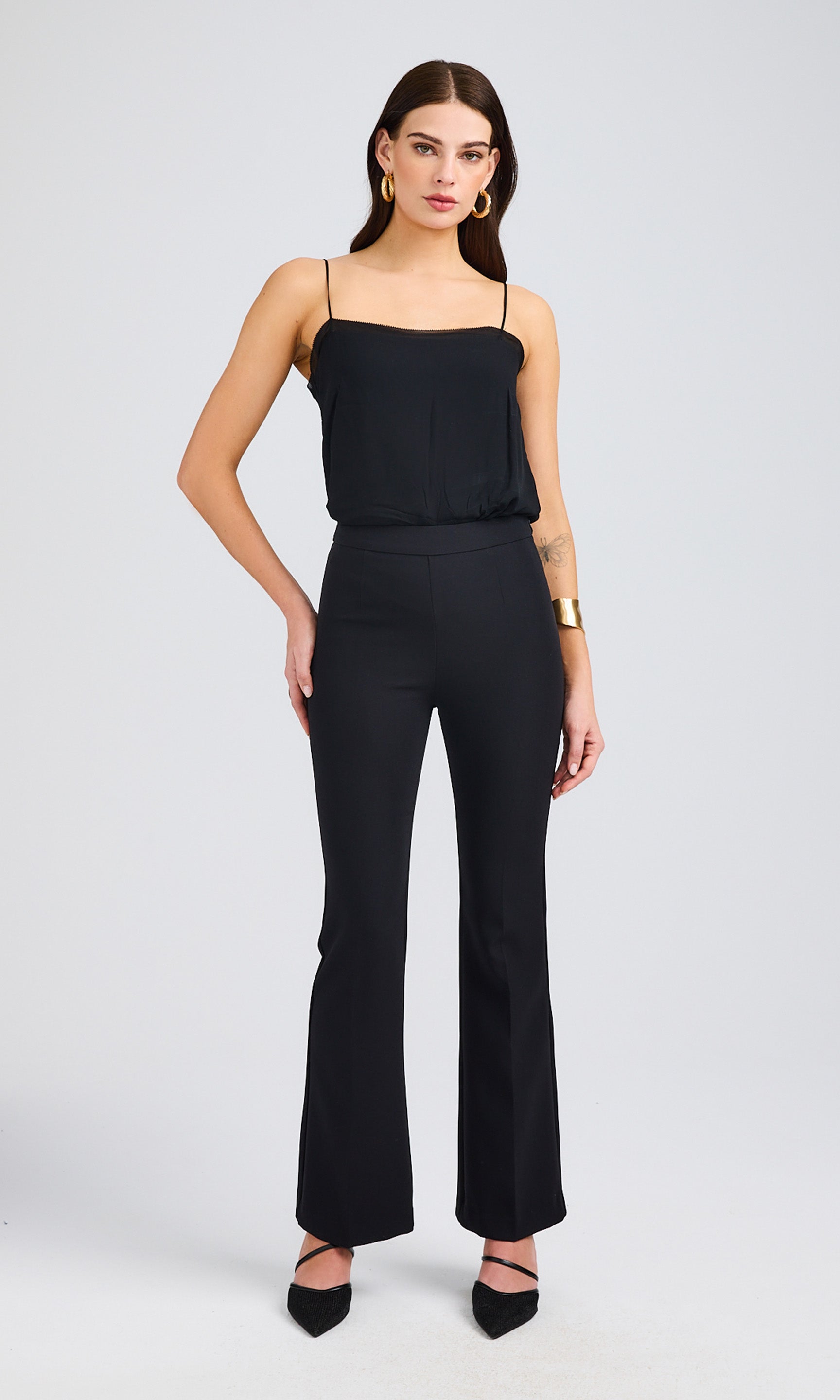 A full-body view of the model in a sleek black outfit featuring a cami top and flared pants