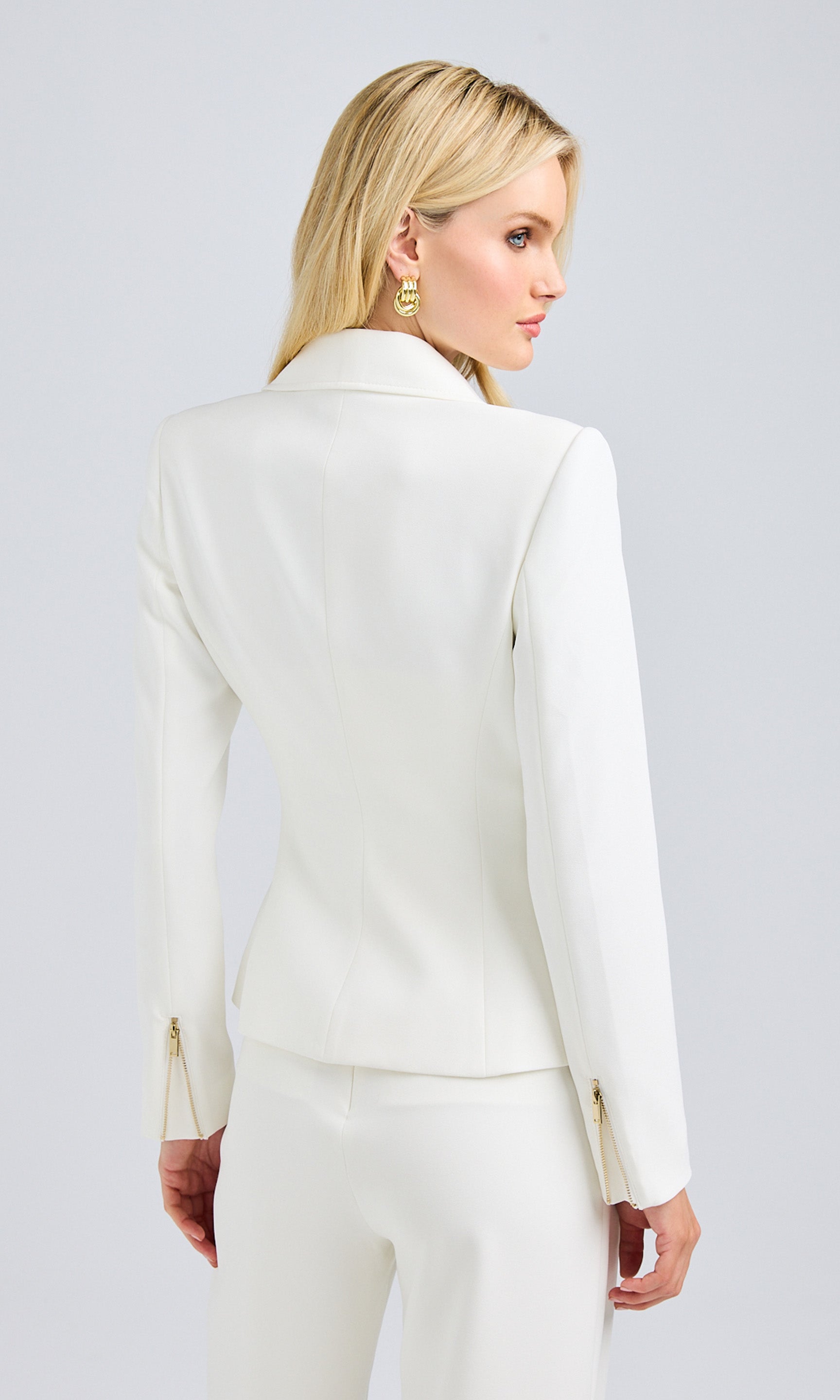 Rear view of a woman in a stylish white suit with gold zipper and buttons, showcasing her outfit.