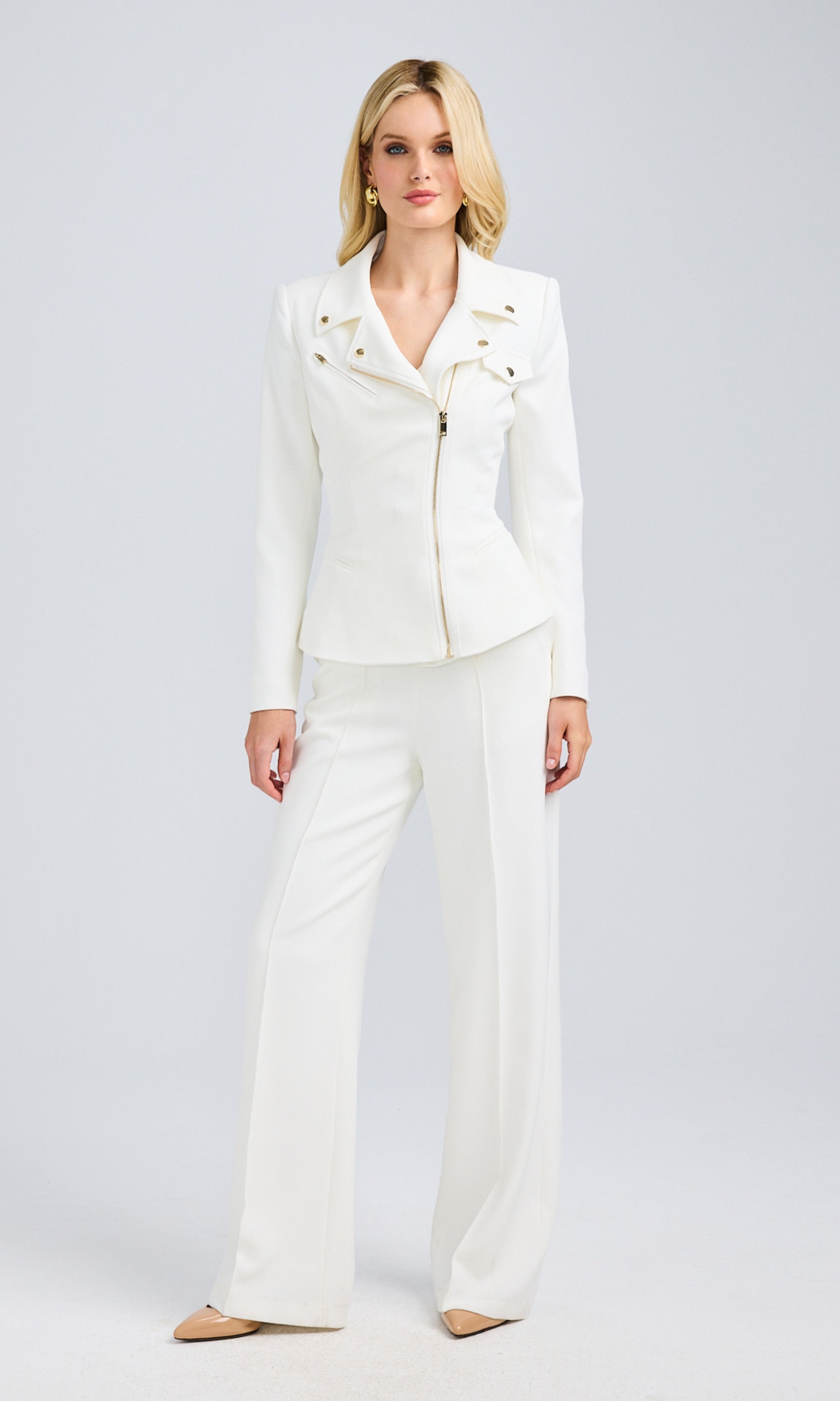 Model poses in a white suit, featuring a moto jacket with gold details and matching pants.
