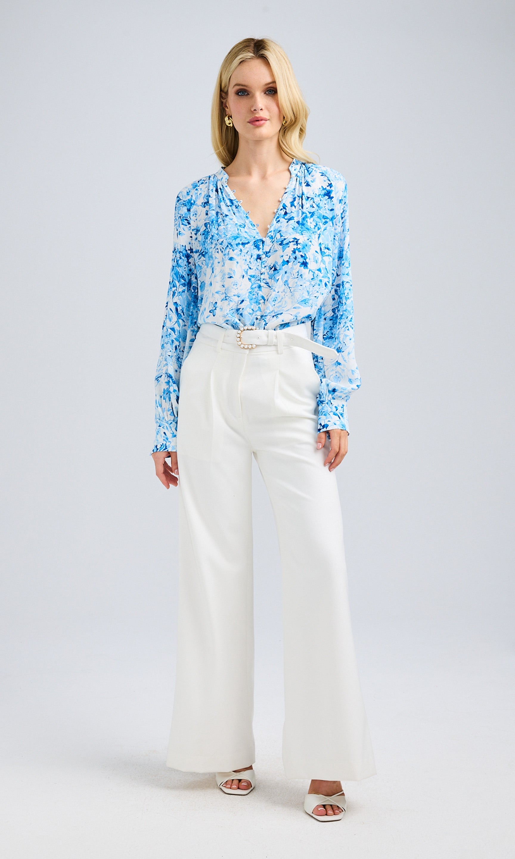 Full-body shot of the model wearing the blue floral blouse with white pants and heels.