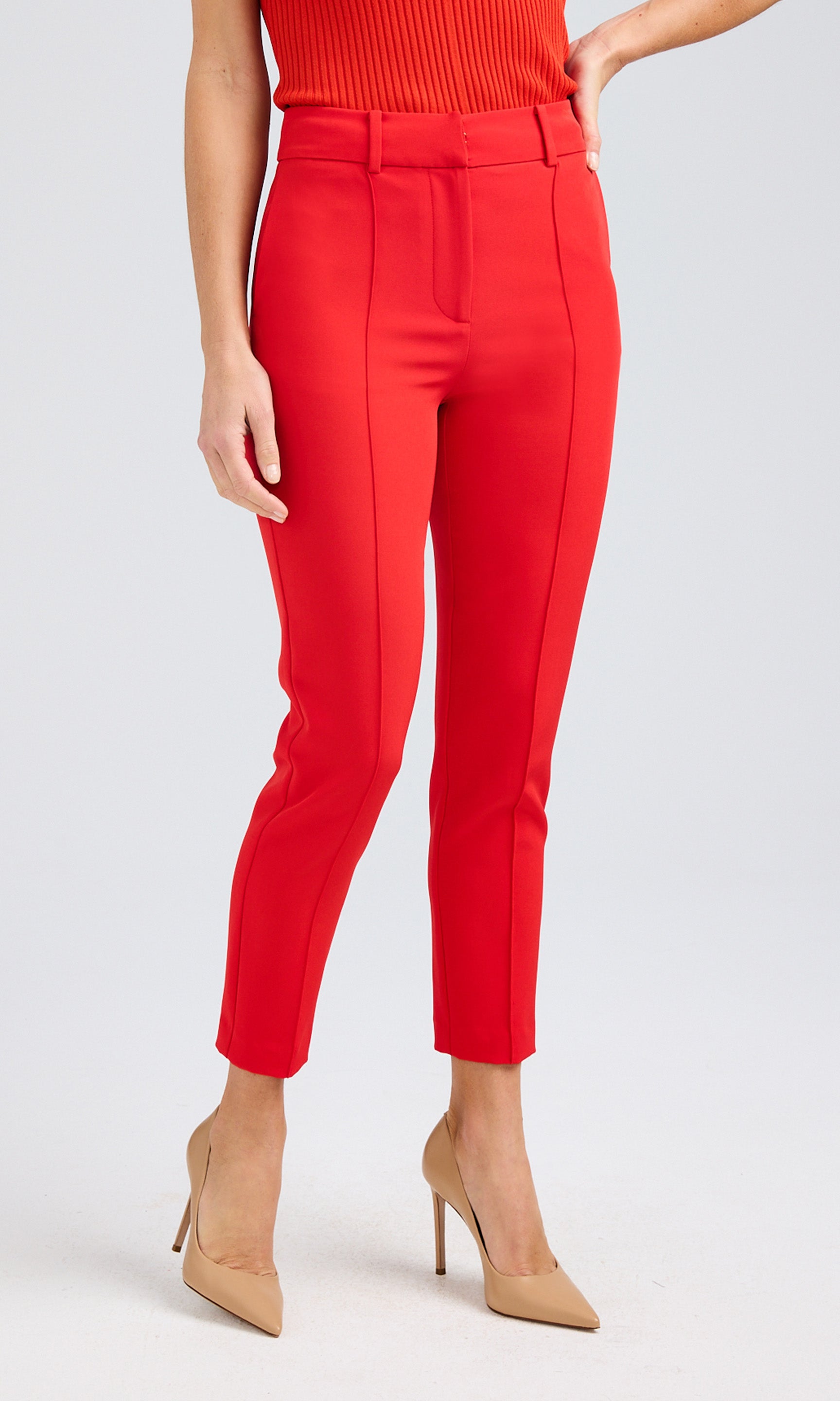 Front view of red crepe pants styled with a ribbed tank, showcasing the sharp fit and clean hemline, paired with nude heels.