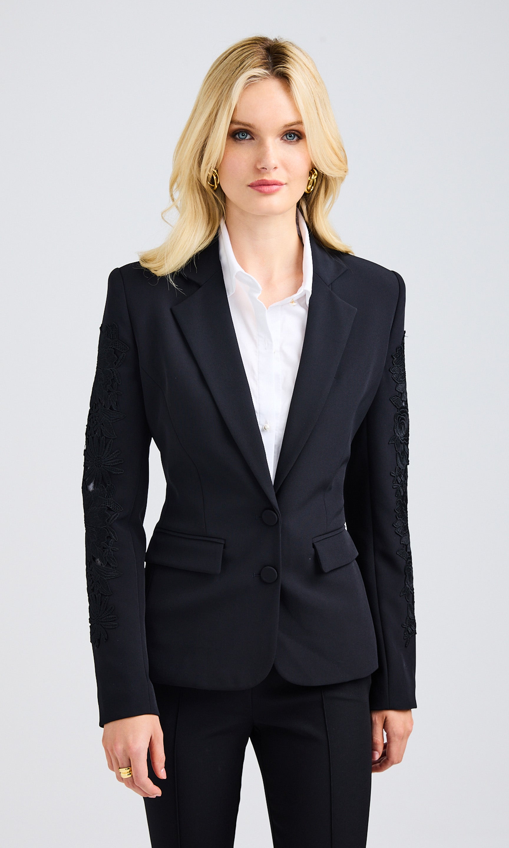 Blonde woman wearing a black single-breasted blazer with lace details along the sleeves.