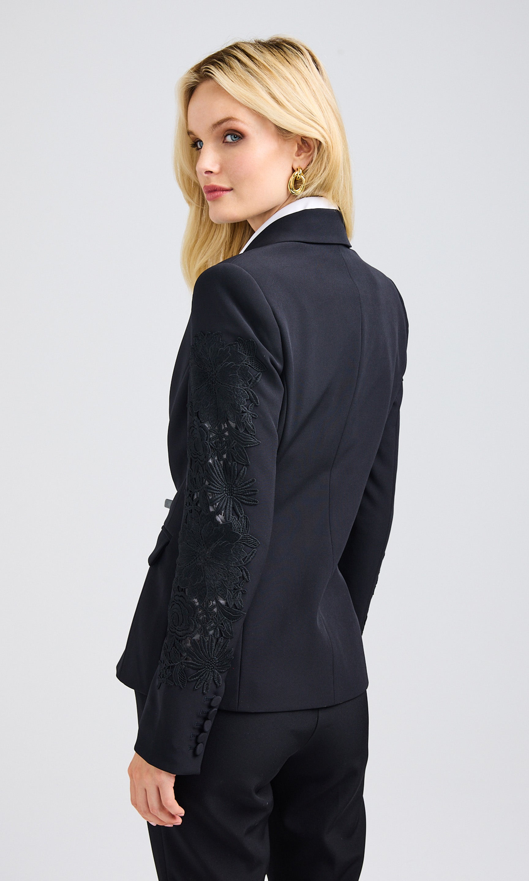 Rear-view of a blonde woman wearing a black lace combo blazer over a white button-up blouse.